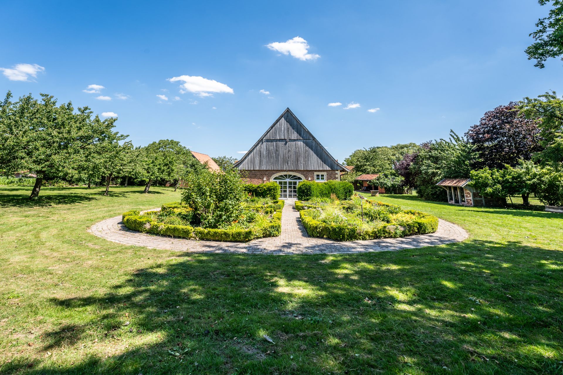 Großer Garten mit rundem Weg und Blumenbeet vor einem Haus mit hohem Giebeldach.