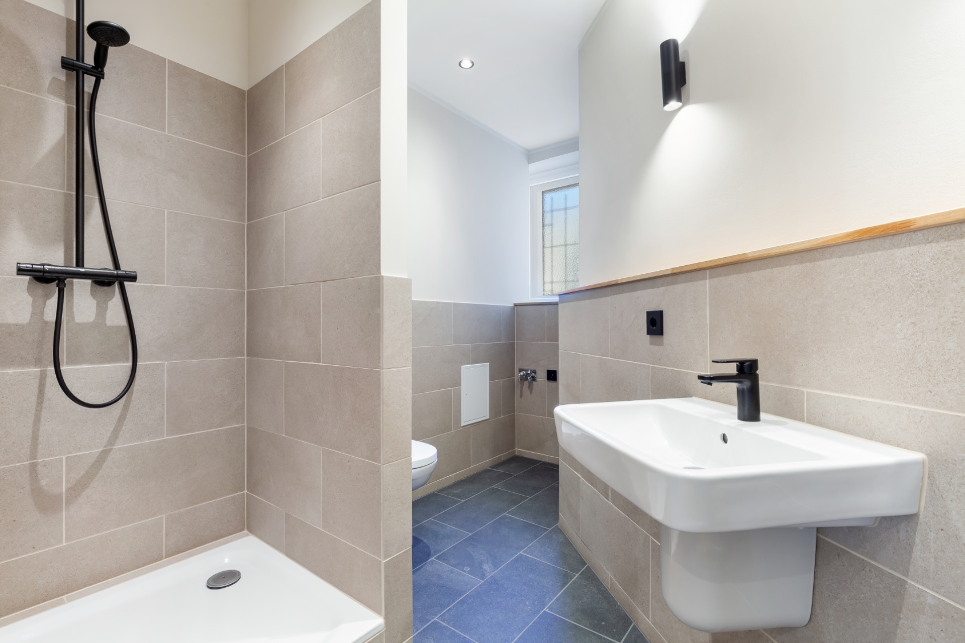 Modernes Badezimmer mit Dusche, Waschbecken, Toilette und Fliesenboden.
