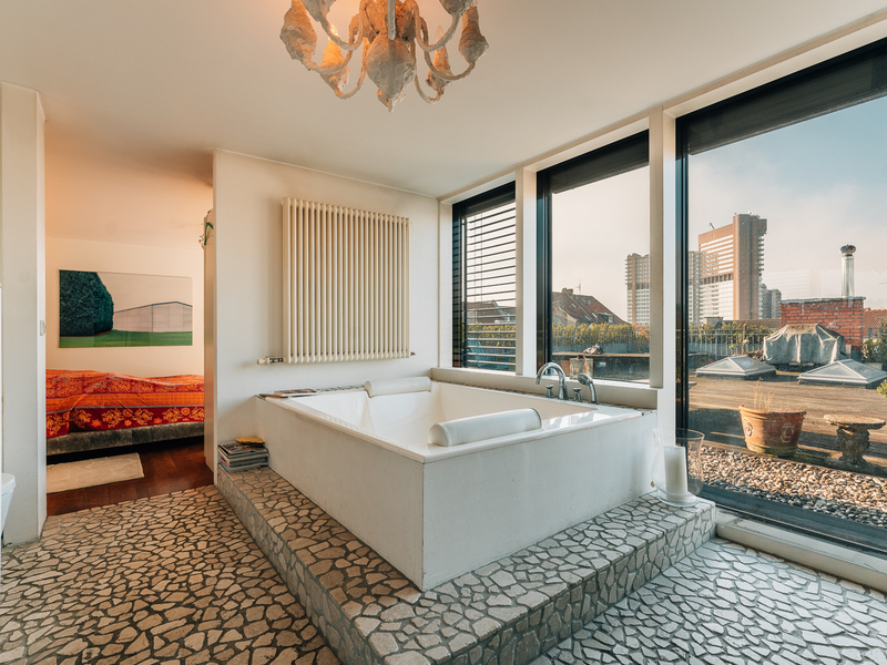 Modernes Bad mit großer Badewanne, Steinfussboden und großen Fenstern mit Stadtblick.
