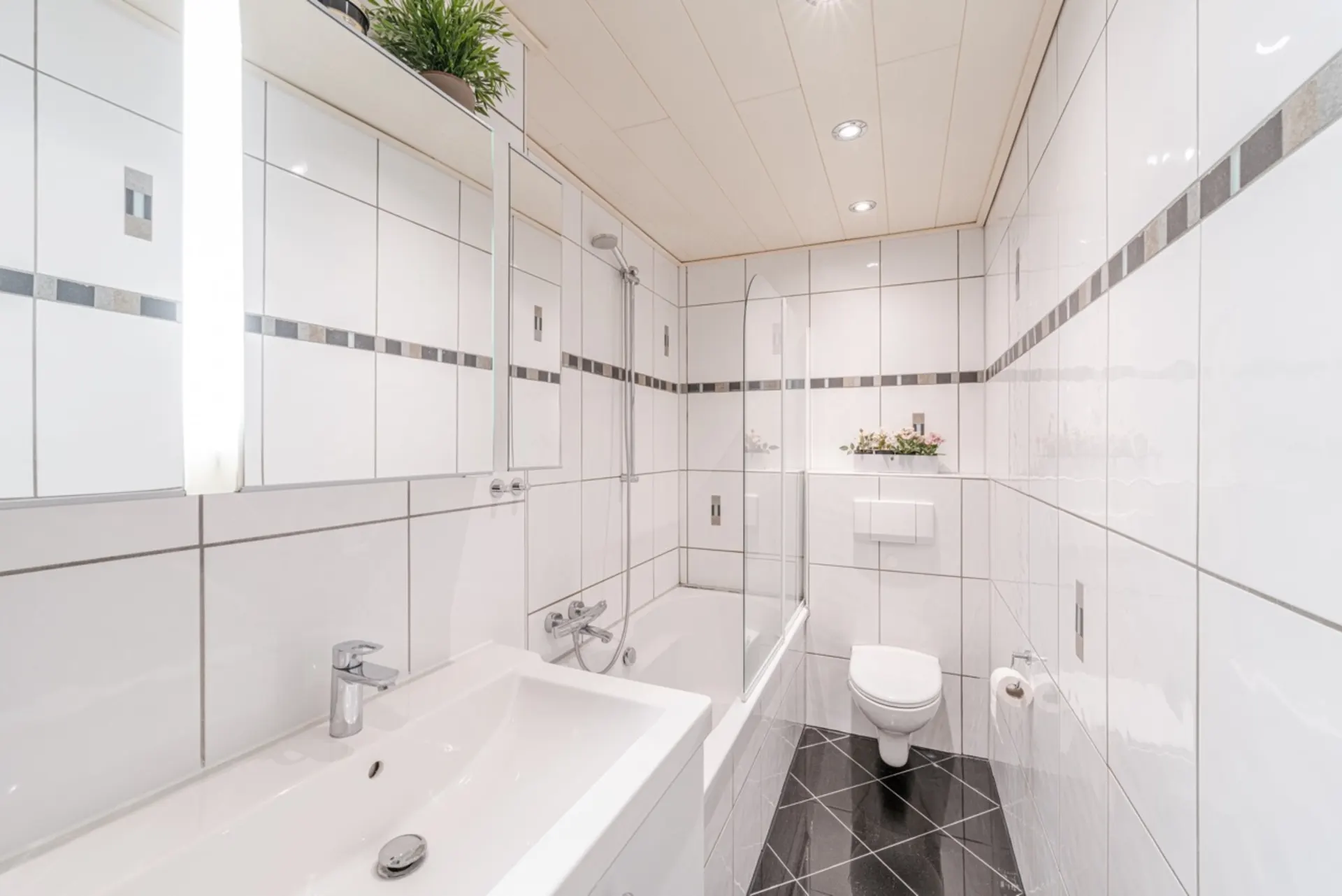 Modernes Badezimmer mit weiß gefliesten Wänden, Badewanne, WC, Waschbecken und Spiegel.