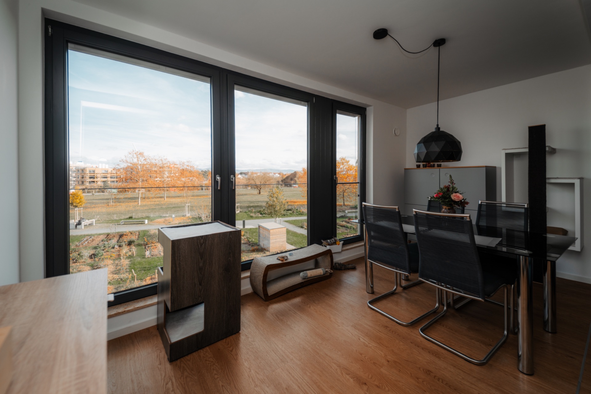 Essbereich mit vier Stühlen, großem Fenster und Blick auf einen Garten.