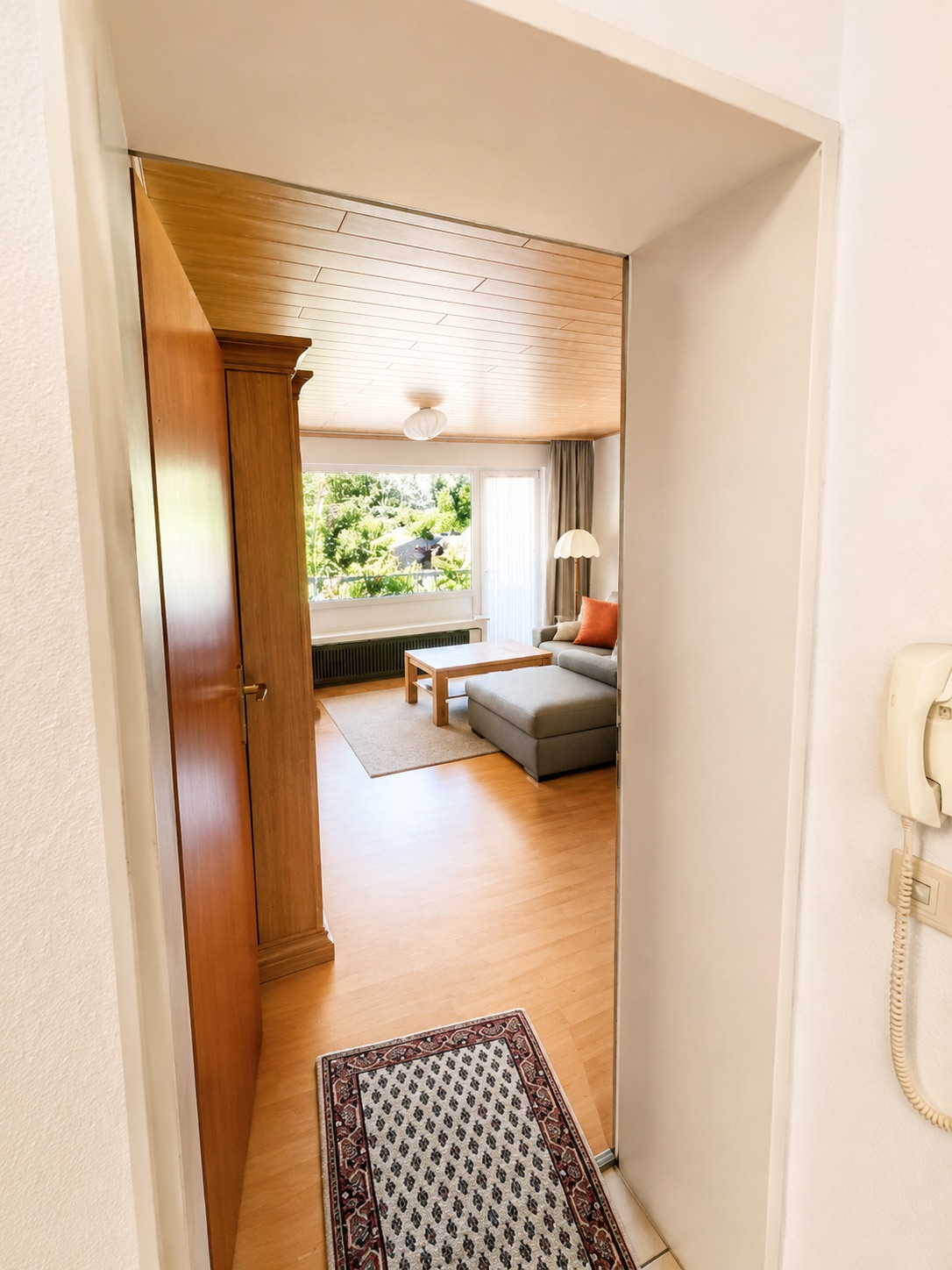 Blick durch einen Flur in ein helles Wohnzimmer mit Sofa, Couchtisch und großem Fenster.