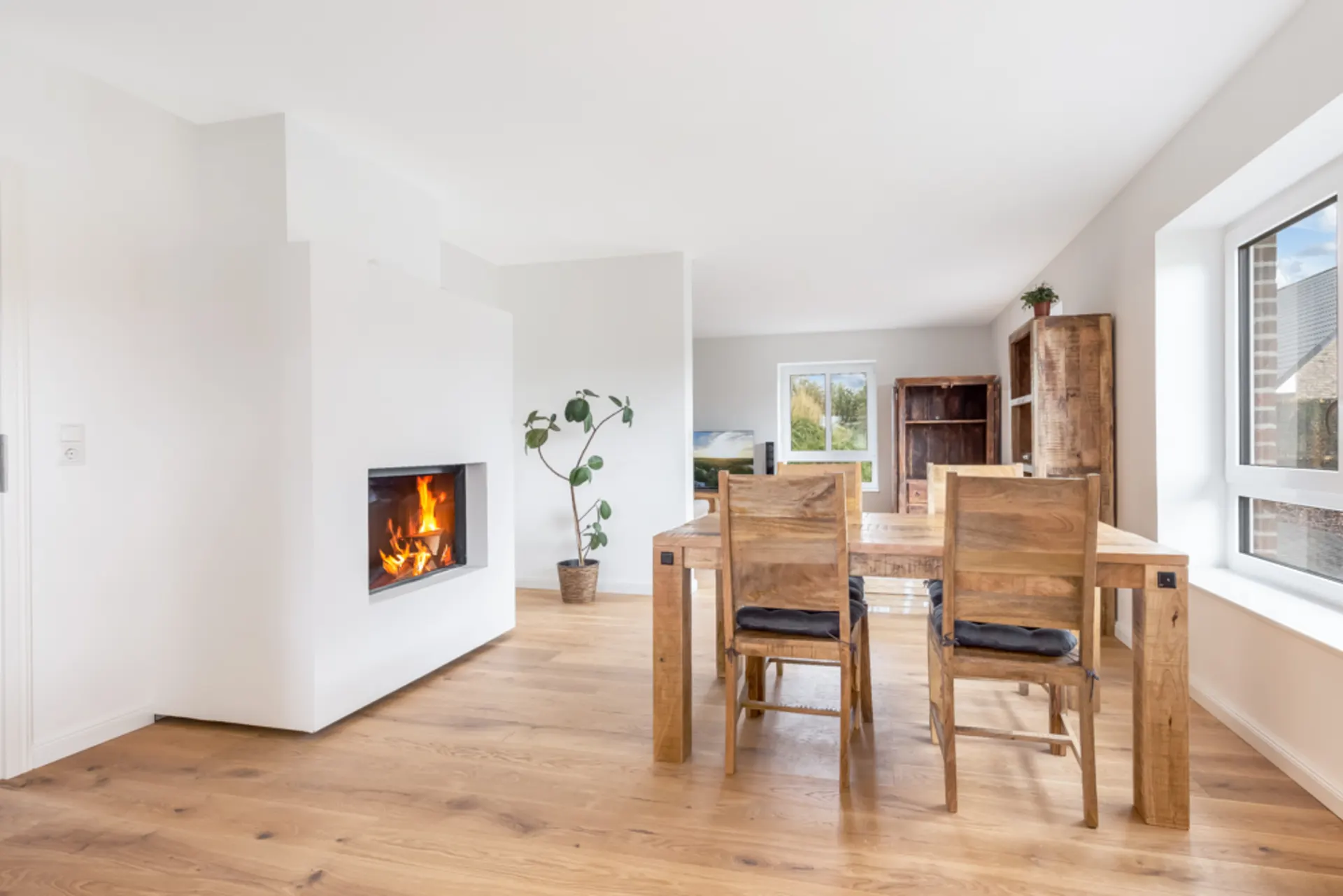 Helles Esszimmer mit Holztisch, vier Stühlen, Kamin und großen Fenstern.