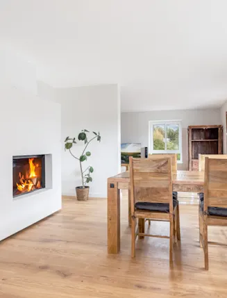 Helles Esszimmer mit Holztisch, vier Stühlen, Kamin und großen Fenstern.