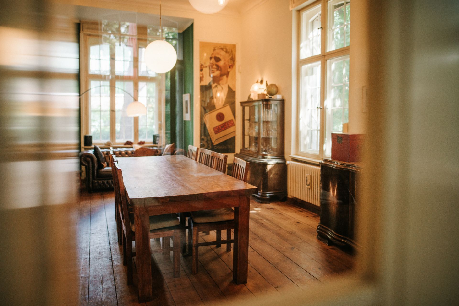Esszimmer mit Holzfußboden, großem Holztisch, Stühlen und großen Fenstern.