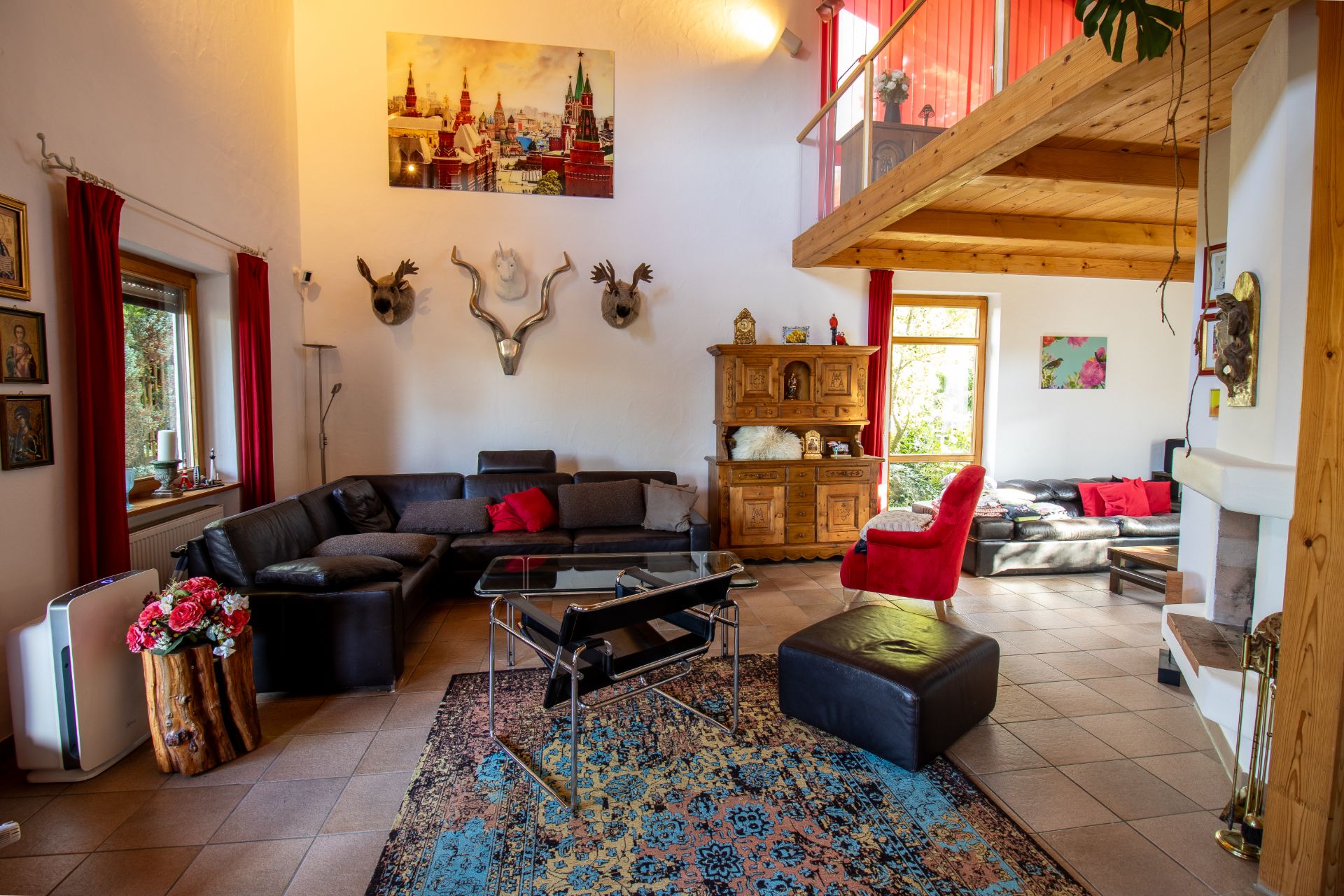 Helles Wohnzimmer mit Ecksofa, rotem Sessel, Teppich, Kamin, Holzregal und Galerie.