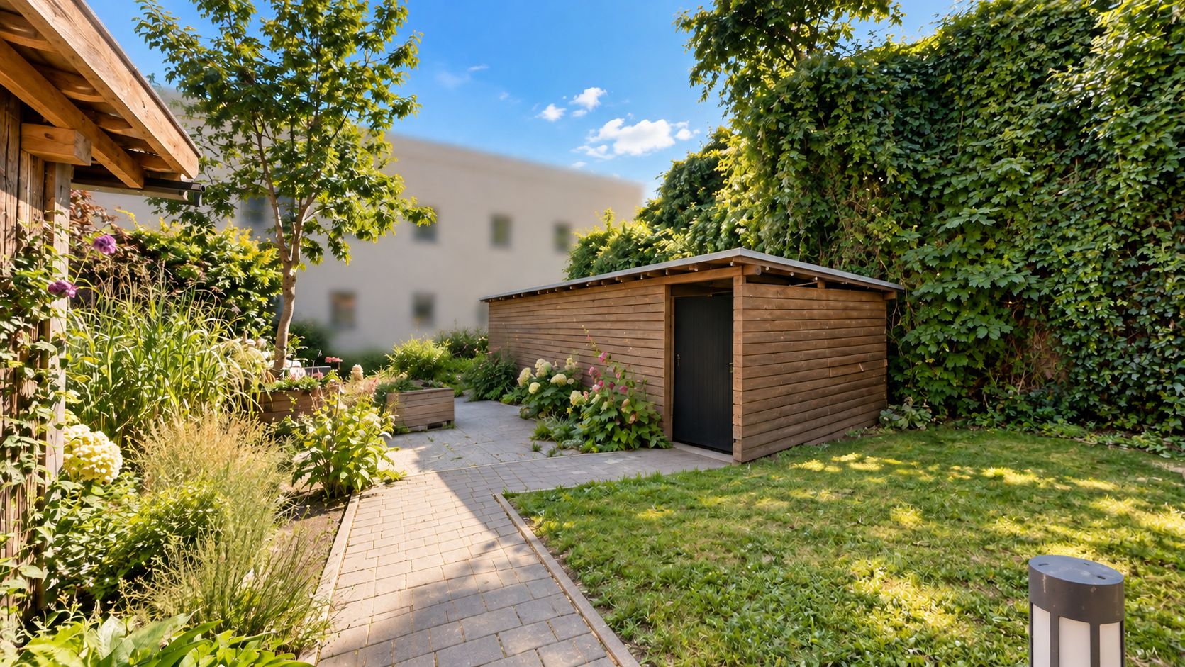 Garten mit Rasen, Holzhütte, Pflanzen und gepflastertem Weg bei Sonnenschein.