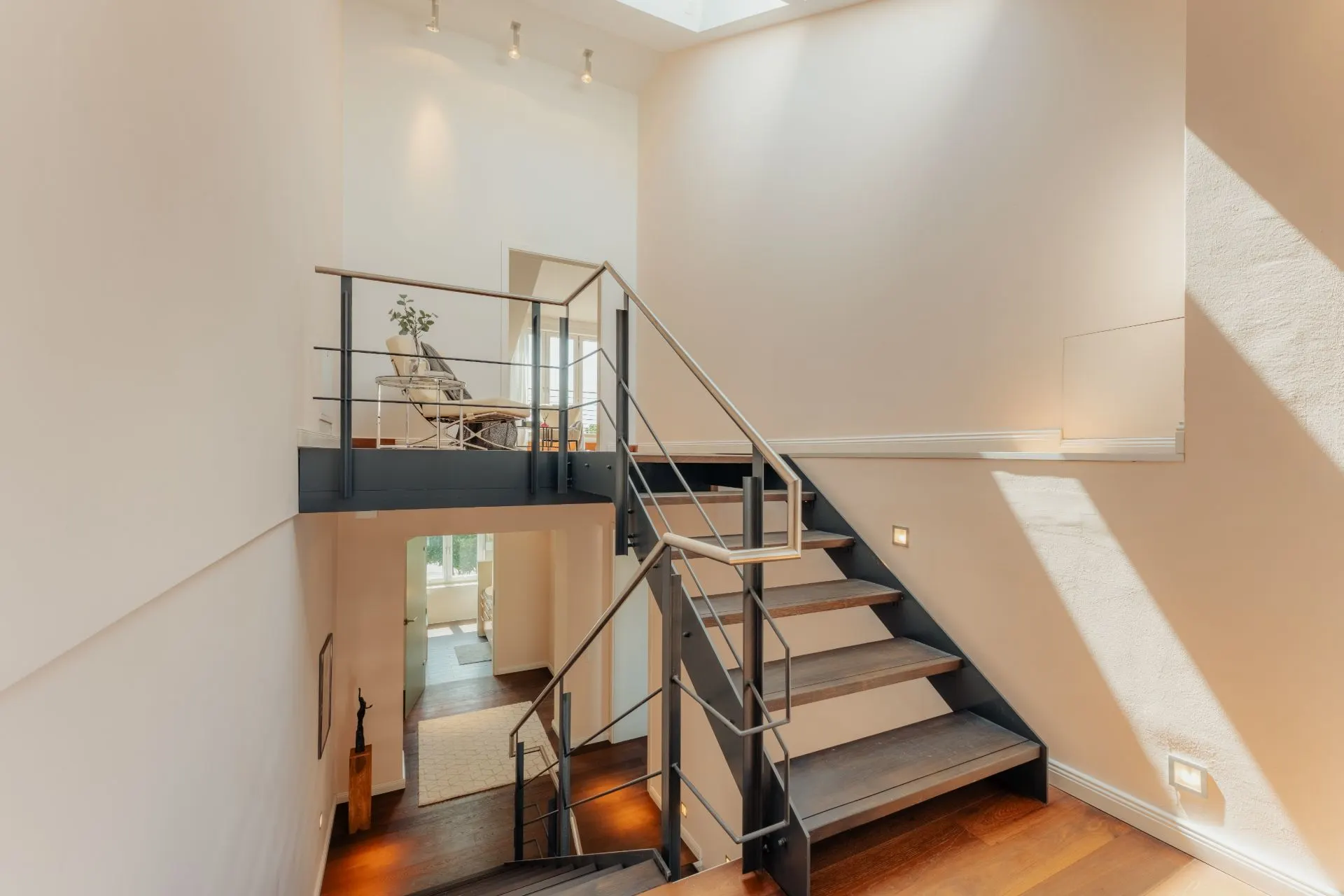 Moderne Treppe mit Metallgeländer in einem hellen Wohnbereich mit Holzboden.