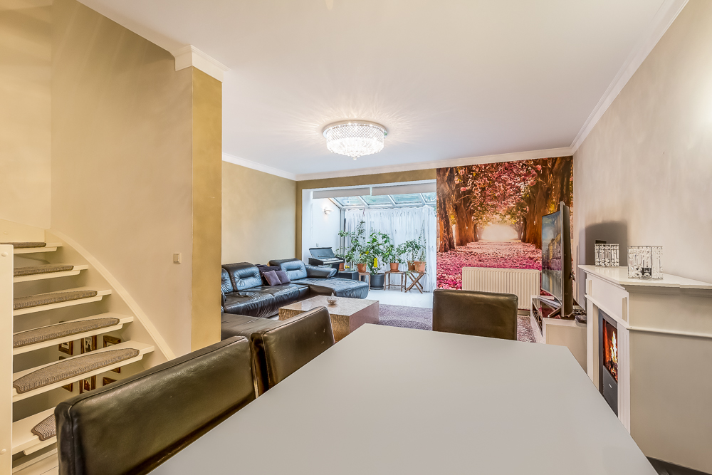Modernes Wohnzimmer mit Ledersofas, Kamin, Esstisch und großem Wandbild eines Parks.