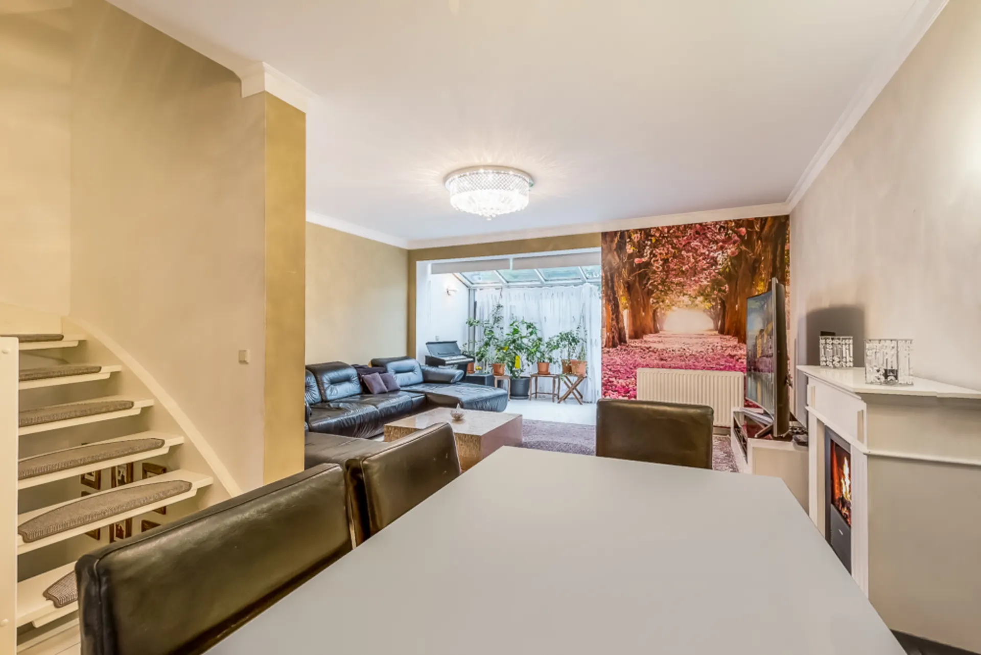 Modernes Wohnzimmer mit Ledersofas, Kamin, Esstisch und großem Wandbild eines Parks.