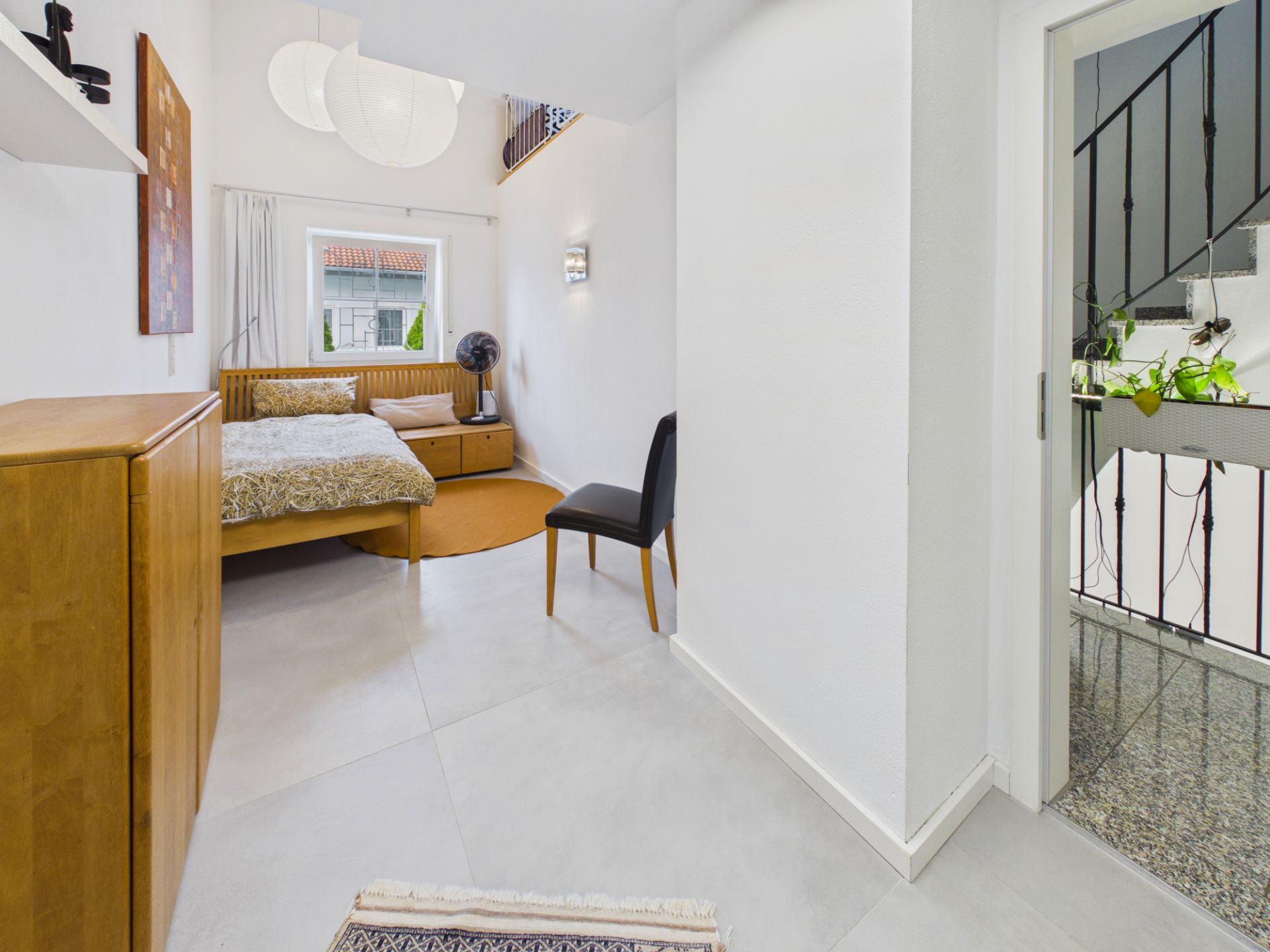 Helles Schlafzimmer mit Holzbett, Schrank, Stuhl und großem Fenster.