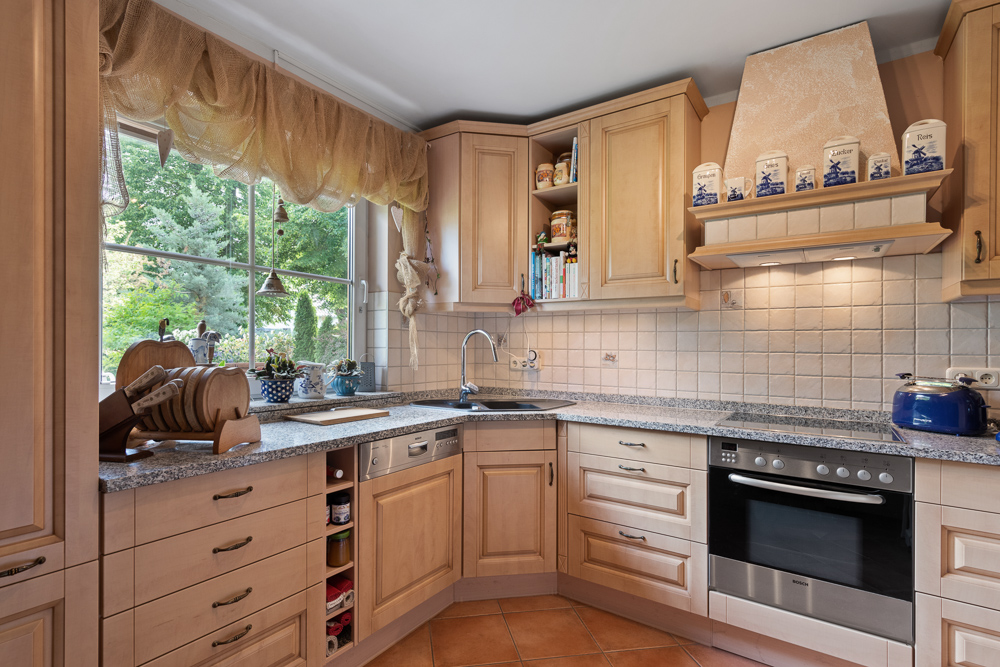 Helle, gemütliche Küche mit Holzschränken, großem Fenster, Herd, Spüle und Dekorationen.