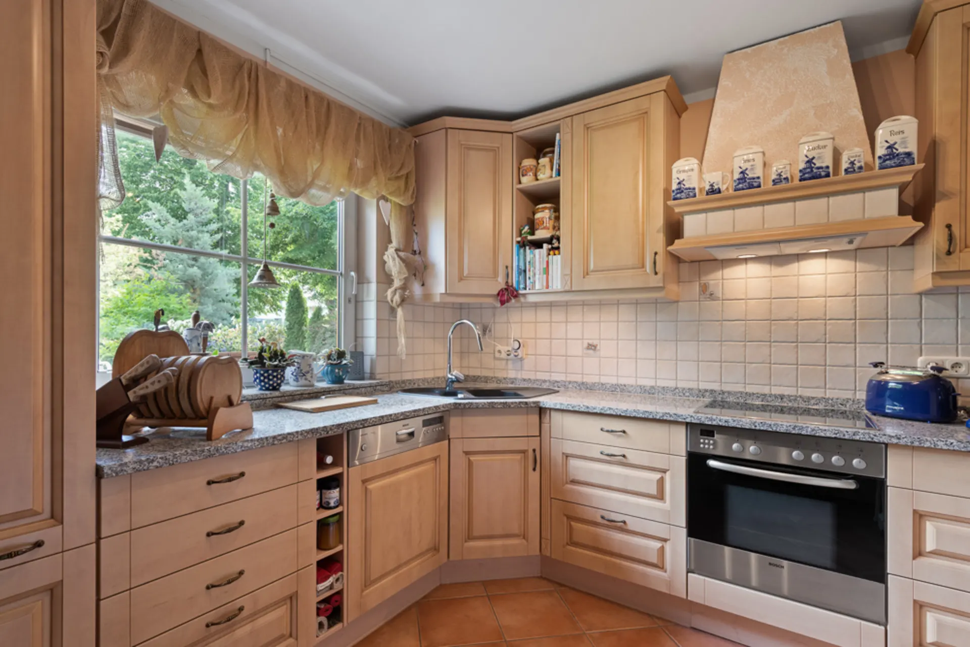 Helle, gemütliche Küche mit Holzschränken, großem Fenster, Herd, Spüle und Dekorationen.