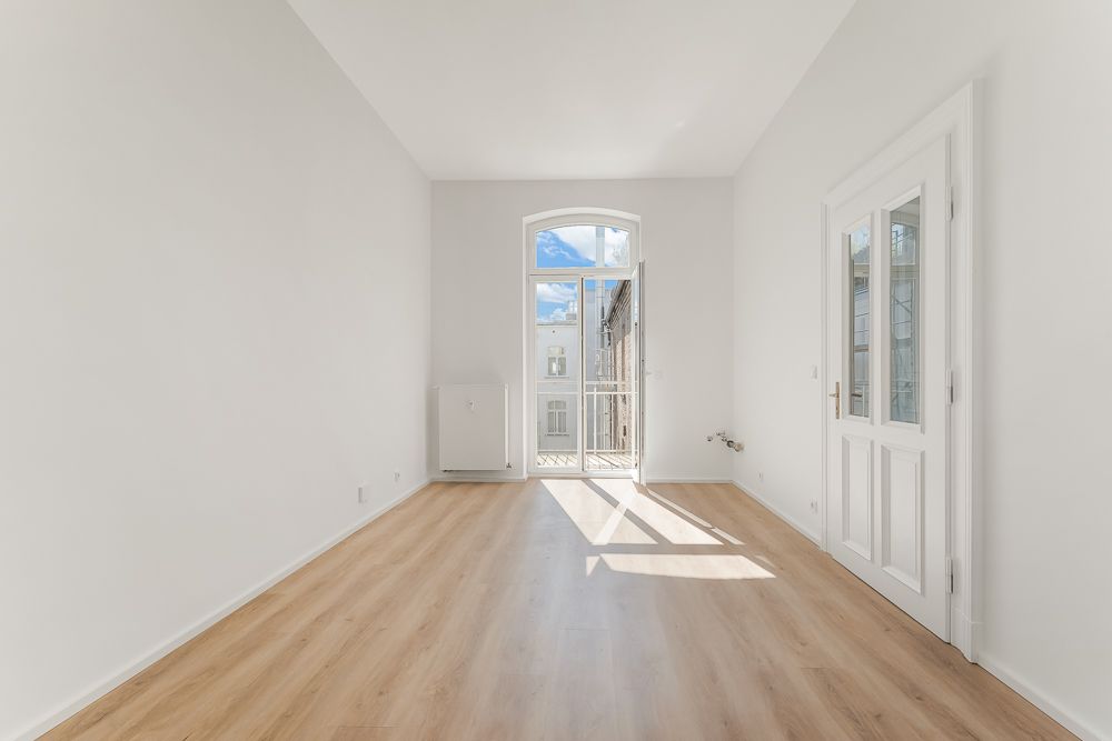 Heller, leerer Raum mit Holzfußboden, weißen Wänden und Balkontür.