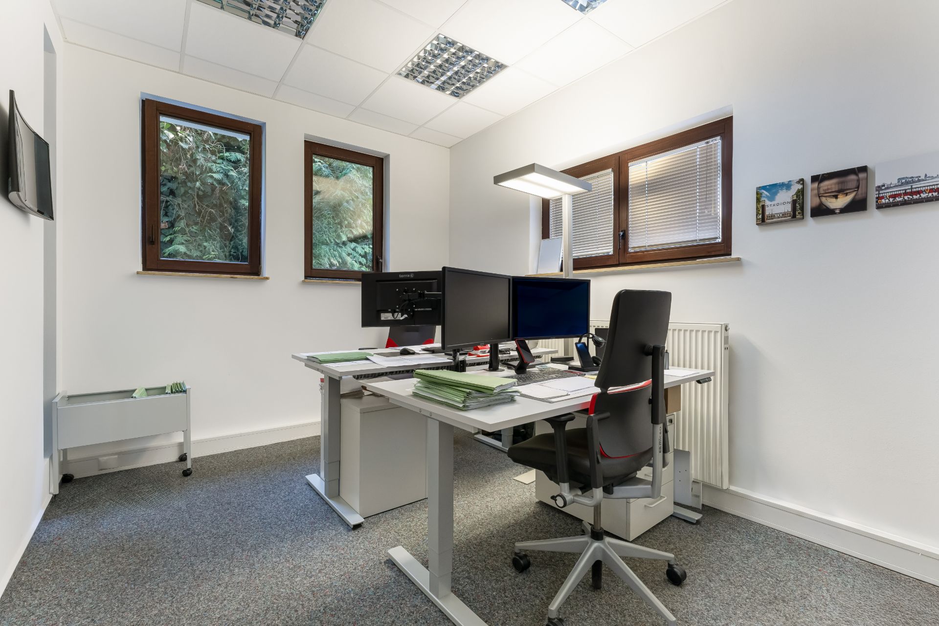 Modernes Arbeitszimmer mit Schreibtisch, Bürostuhl, Monitoren und Fenstern.