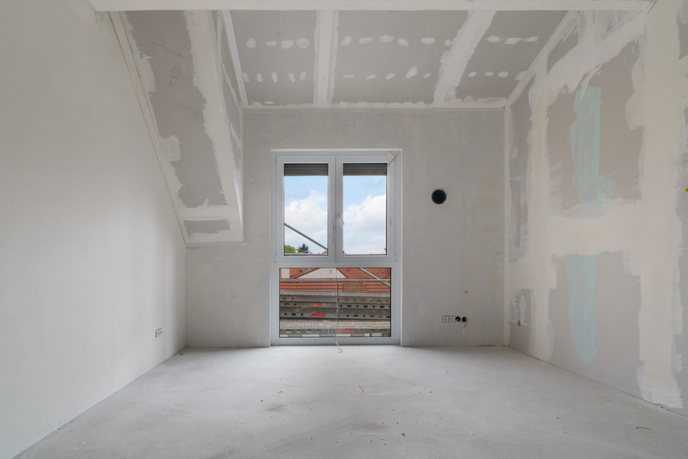 Leerer, unfertiger Raum mit Fenster und sichtbaren Bauarbeiten an den Wänden.