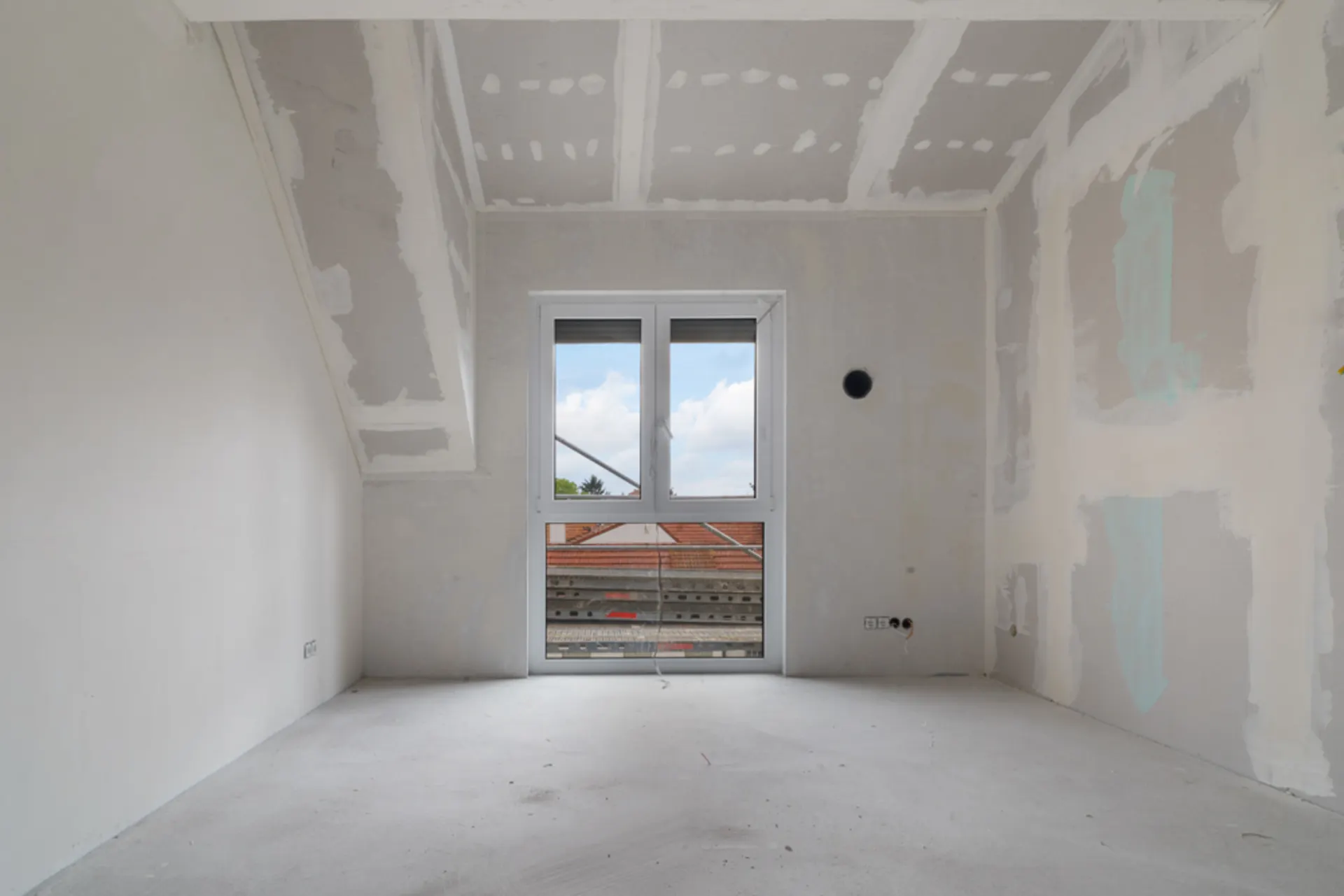 Leerer, unfertiger Raum mit Fenster und sichtbaren Bauarbeiten an den Wänden.