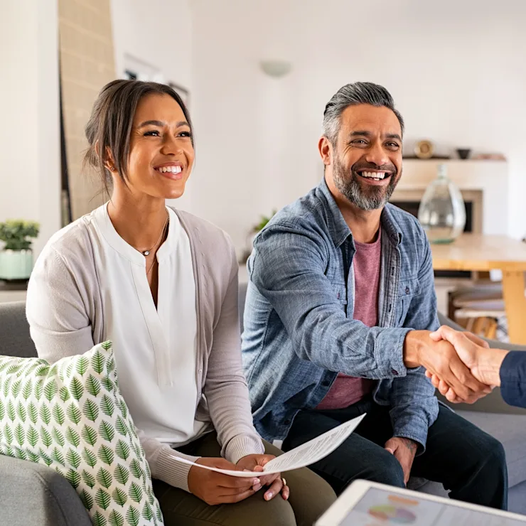 Ein Paar sitzt auf dem Sofa in einem Wohnzimmer, der Mann schüttelt einer Frau die Hand.