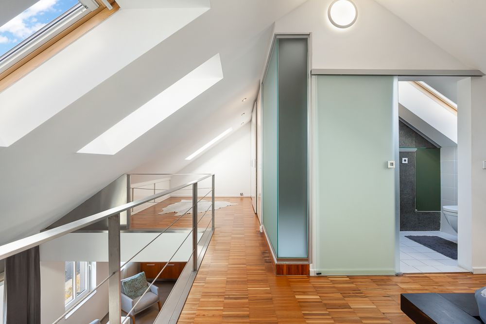 Helle Dachgeschosswohnung mit Parkettboden, Glasgeländer und modernem Badezimmer.