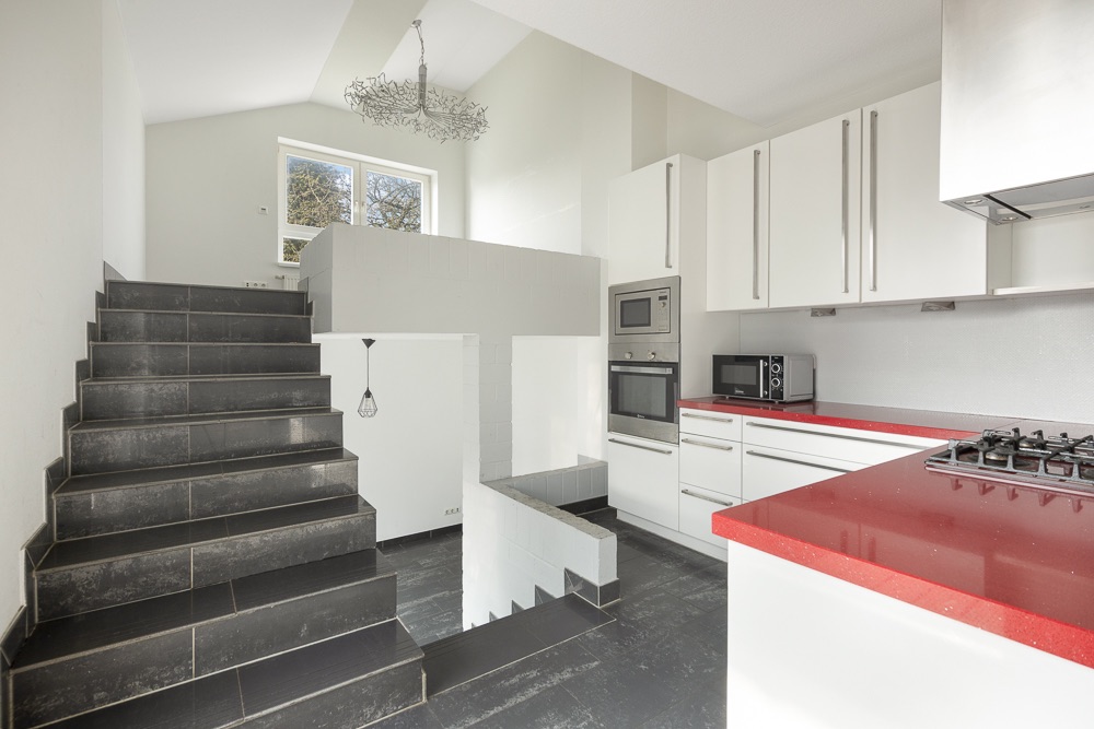 Moderne Küche mit weißen Schränken, roter Arbeitsplatte und schwarzer Treppe.