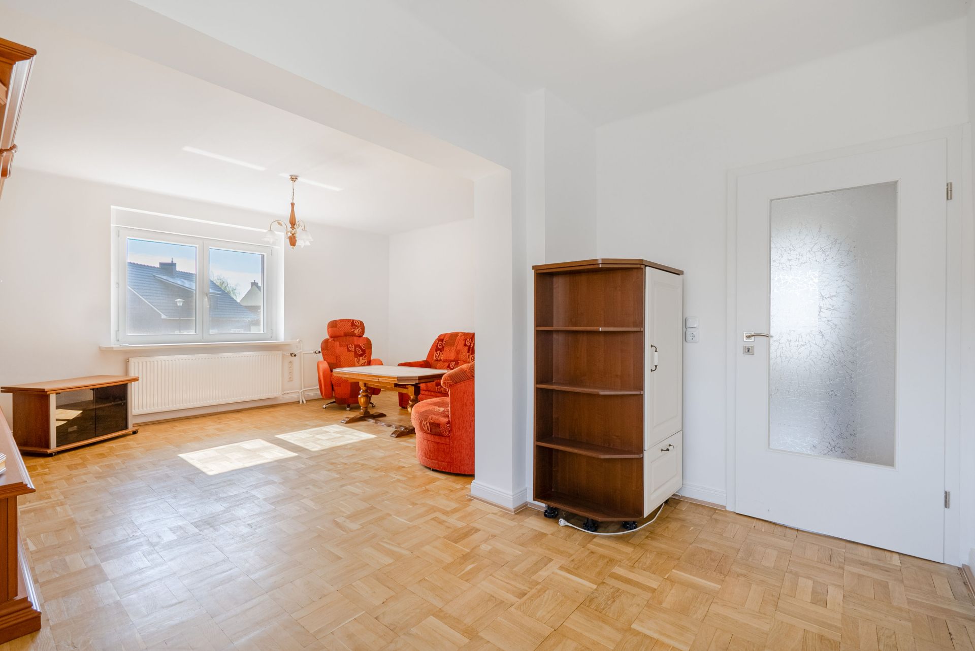 Helles Wohnzimmer mit Parkettboden, roten Sesseln, Couchtisch und großem Fenster.