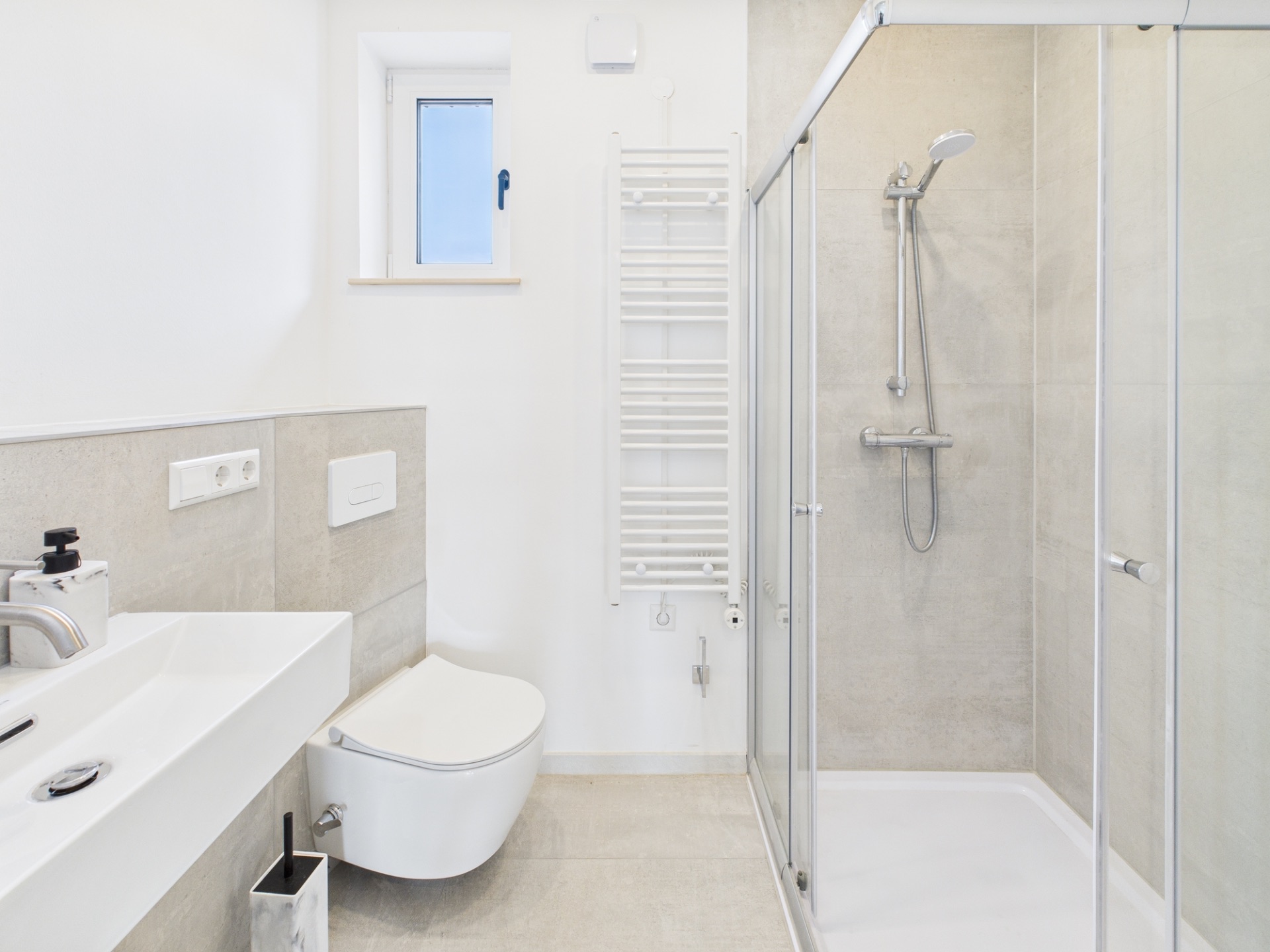 Helles Badezimmer mit Dusche, Wandtoilette, Waschbecken und kleinem Fenster.