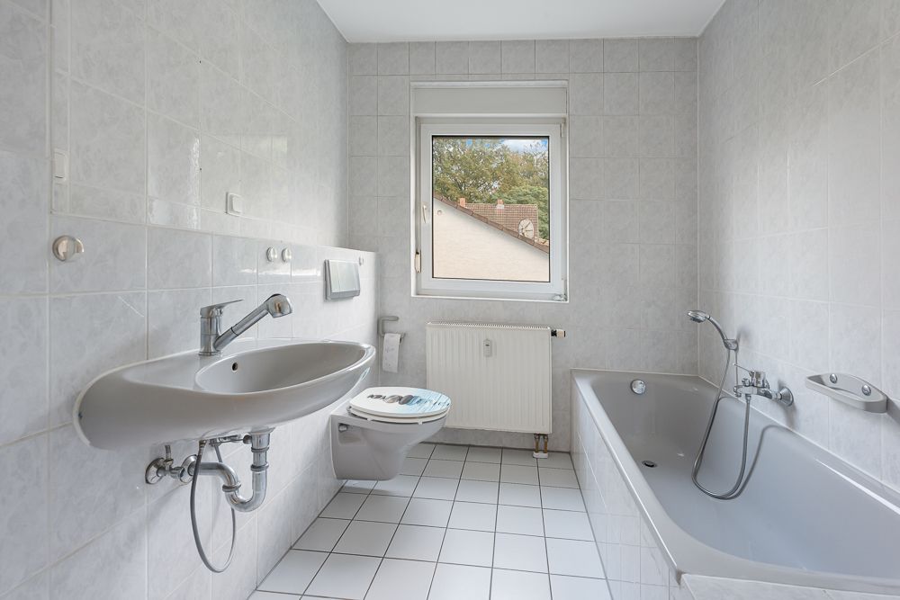 Helles Badezimmer mit Badewanne, Waschbecken, WC und Fenster, komplett gefliest.