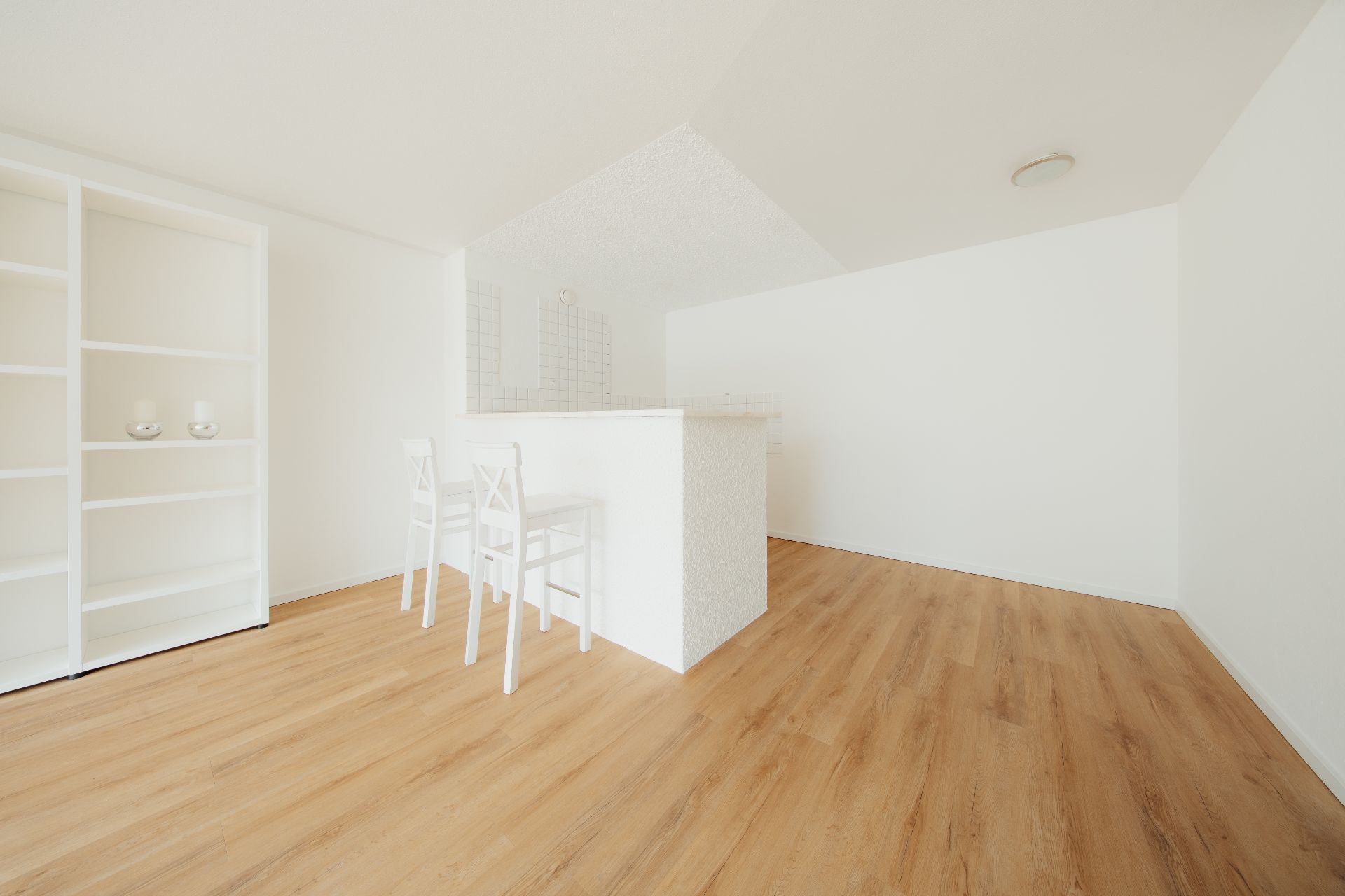 Heller Raum mit Holzfußboden, weißem Regal und zwei weißen Stühlen an einer Theke.