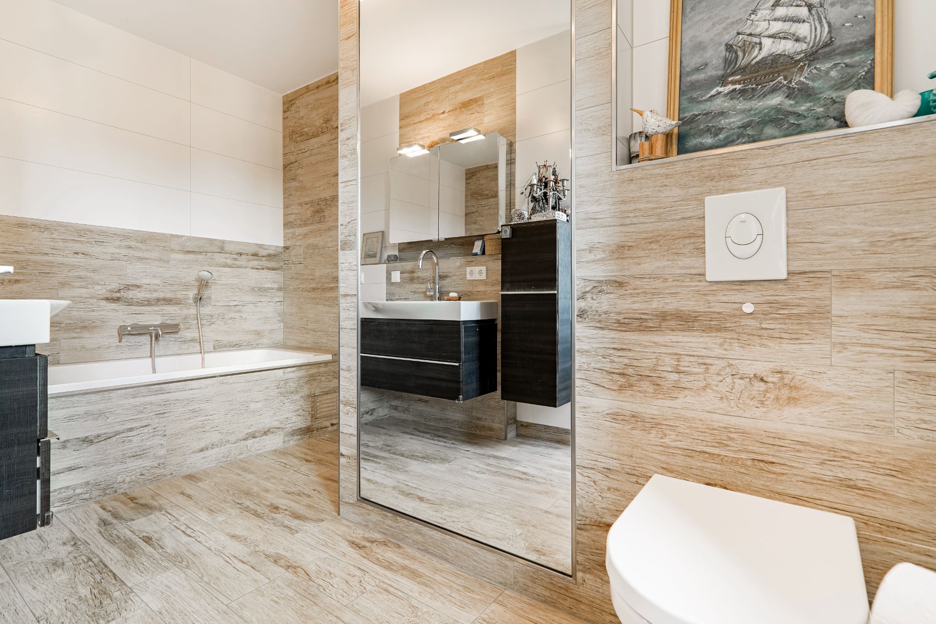 Modernes Badezimmer mit Badewanne, Spiegel, Waschbecken und WC auf holzfarbenen Fliesen.