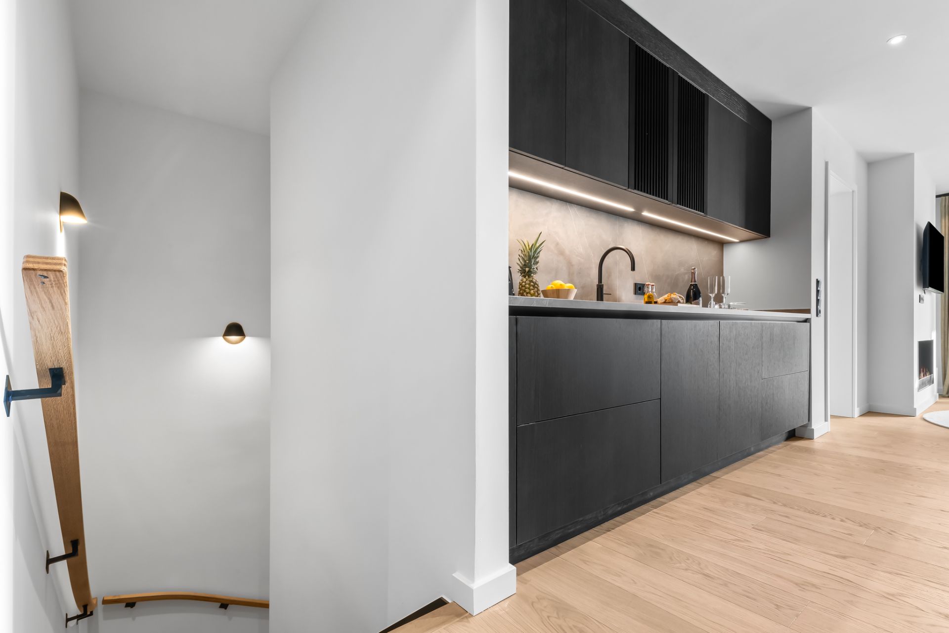Moderne Küche mit dunklen Schränken, Holzfußboden und abgehender Treppe links.