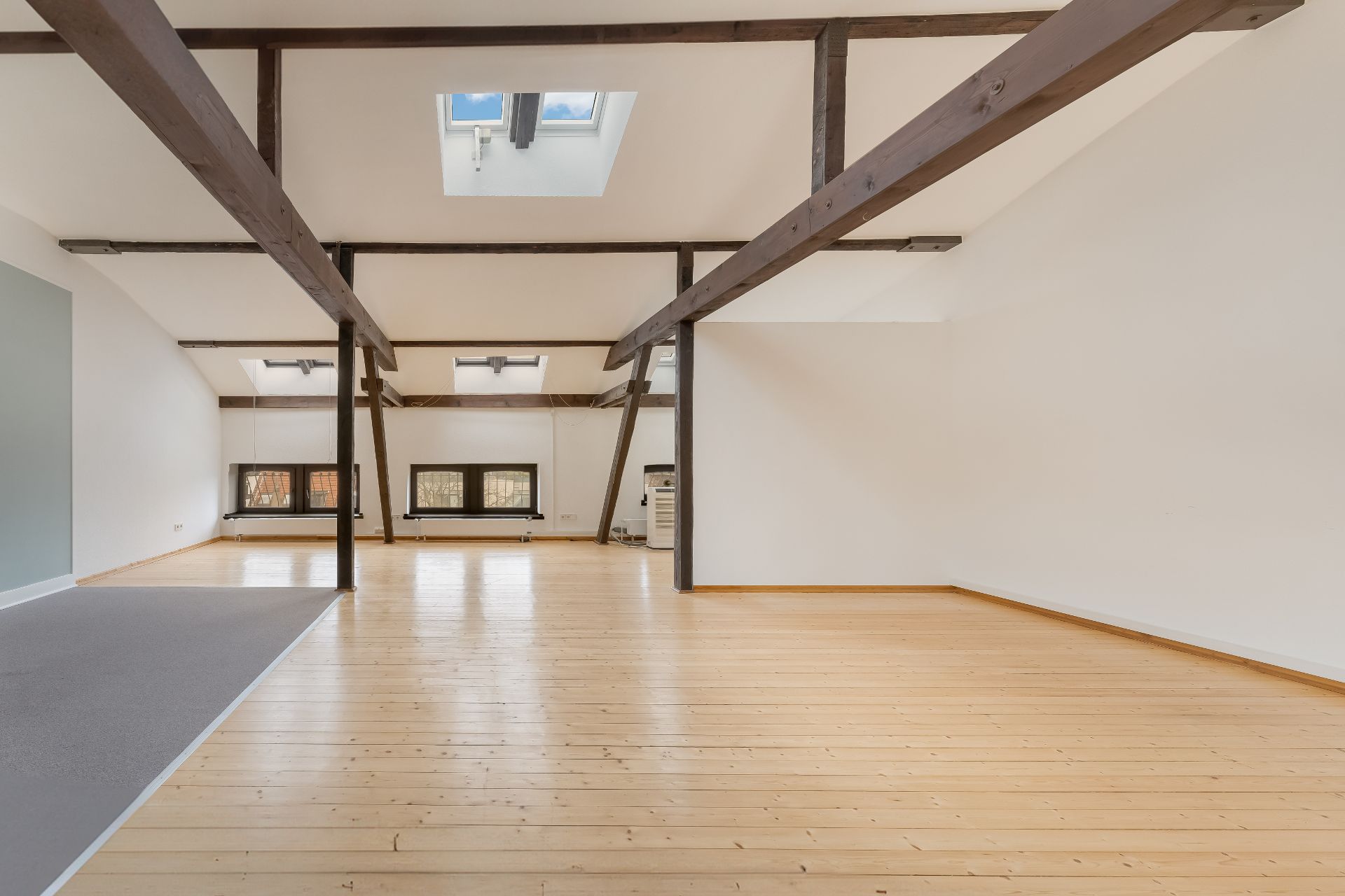 Heller Raum mit Holzboden, sichtbaren Deckenbalken und Dachfenstern.