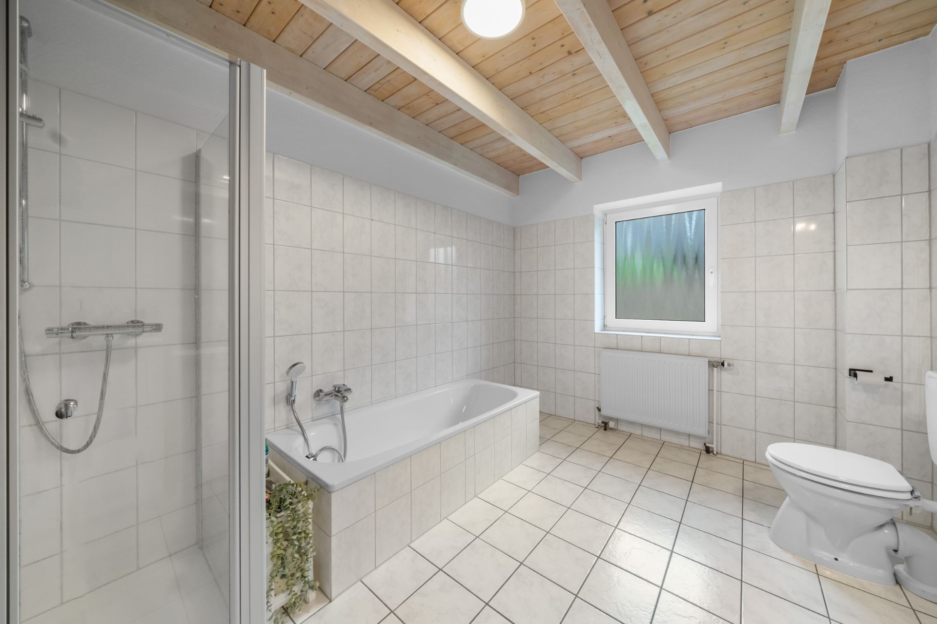 Helles Badezimmer mit Dusche, Badewanne, WC, Fenster und Fliesenboden.