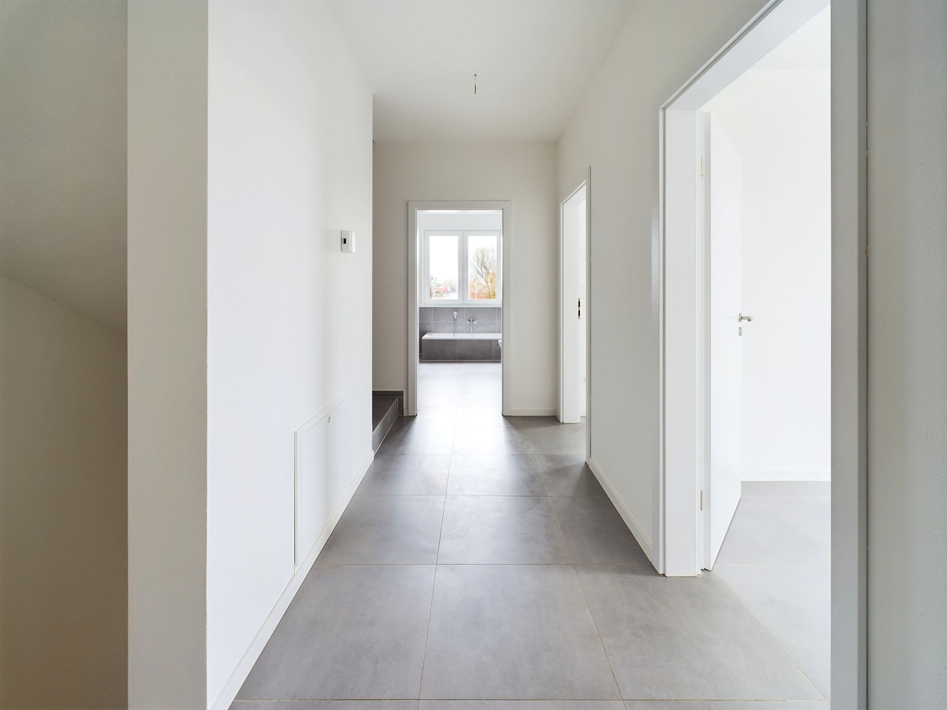 Heller Flur mit Fliesenboden, Türen zu weiteren Zimmern und Fenster am Ende des Gangs.