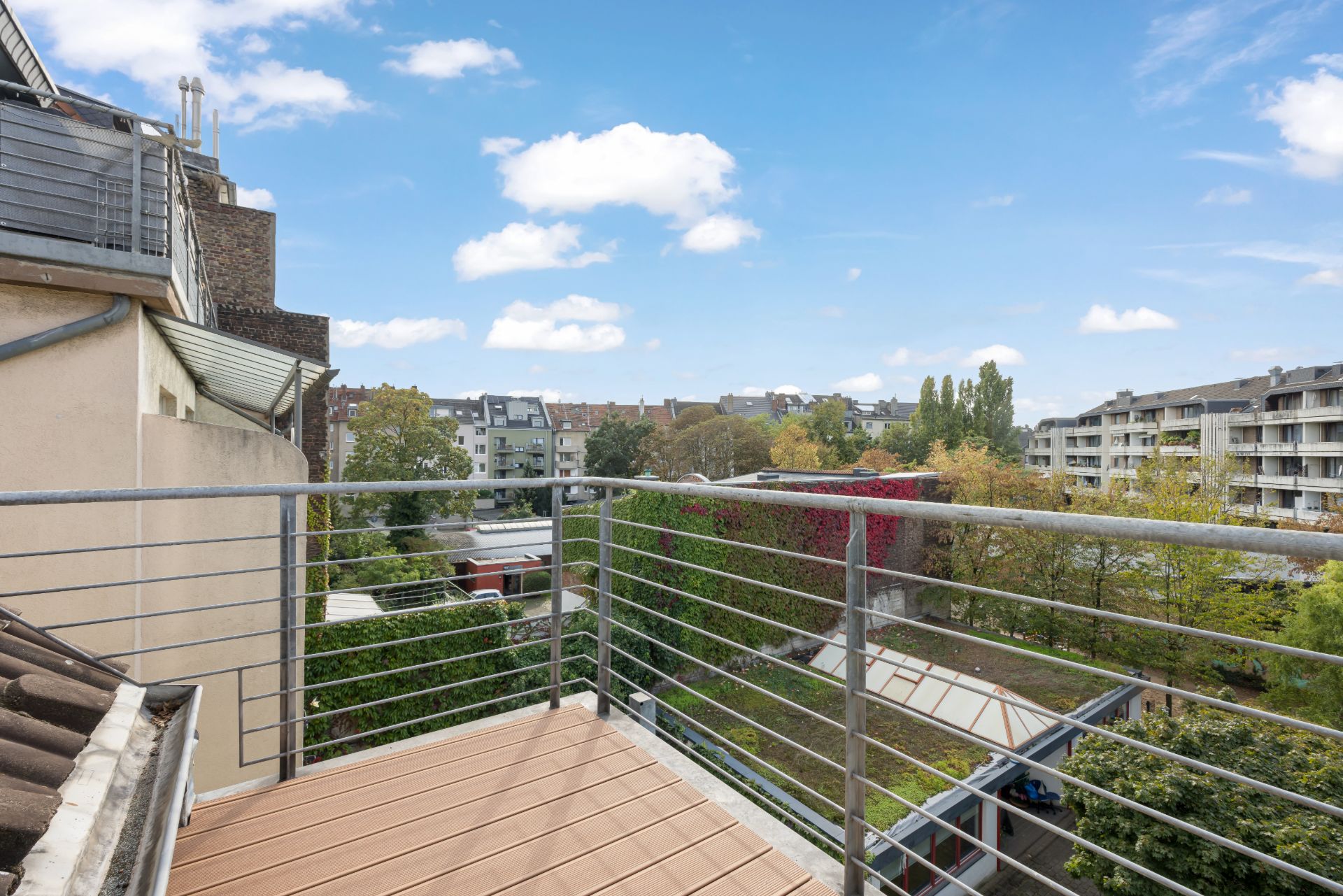 Balkon mit Metallgeländer und Blick auf einen grünen Innenhof und umliegende Wohnhäuser.
