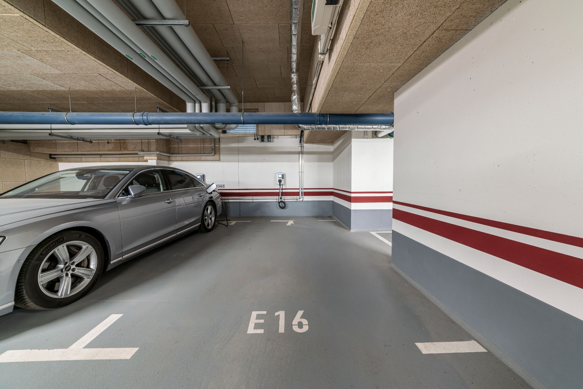 Tiefgaragenstellplatz E16 mit einem geparkten silbernen Auto und einer Ladestation an der Wand.
