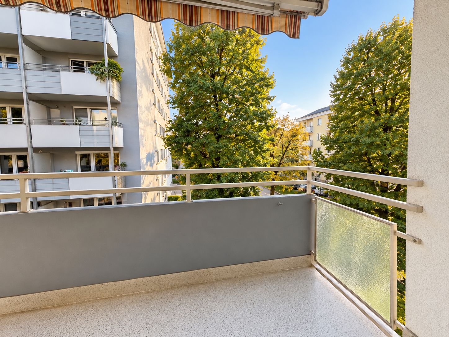Balkon mit Geländer und Markise, Blick auf Bäume und Nachbargebäude.