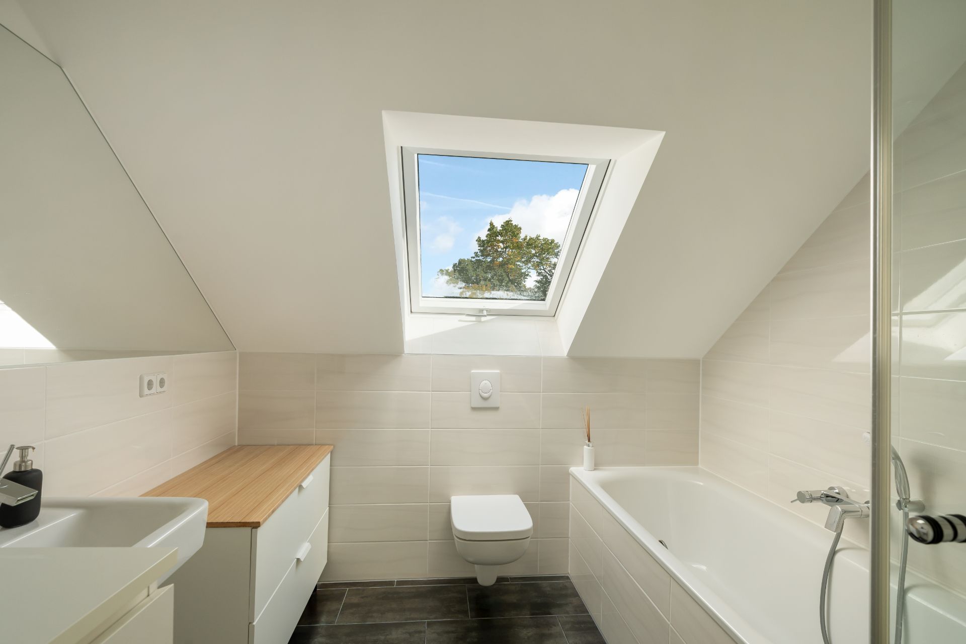Modernes Badezimmer mit Badewanne, Toilette und Dachfenster unter einer Schräge.