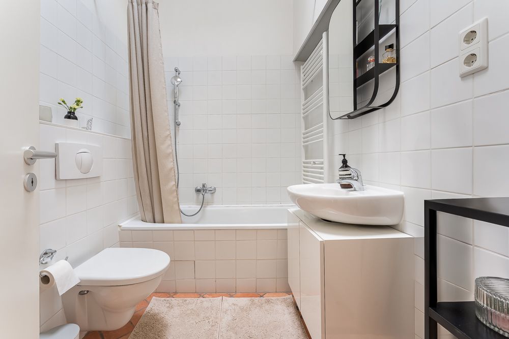 Helles Badezimmer mit Badewanne, WC, Waschbecken und Spiegel an weiß gefliester Wand.