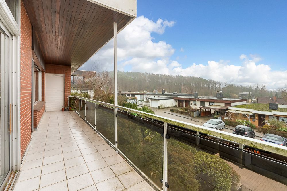 Balkon mit Glasgeländer, Blick auf Straße mit Autos und Häusern, bewölkter Himmel.