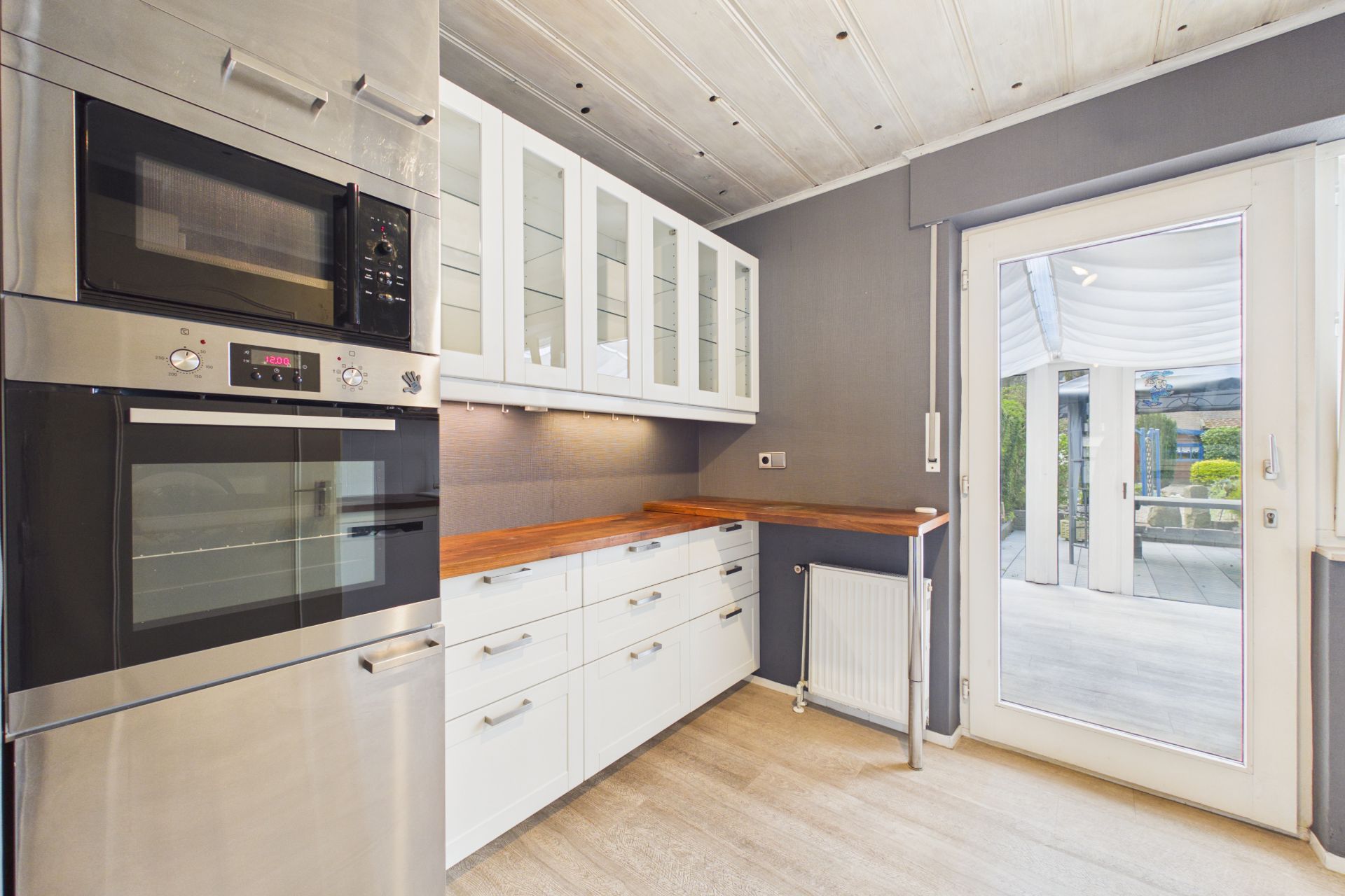 Moderne Küche mit weißen Schränken, Holzarbeitsplatte und Glastür zur Terrasse.