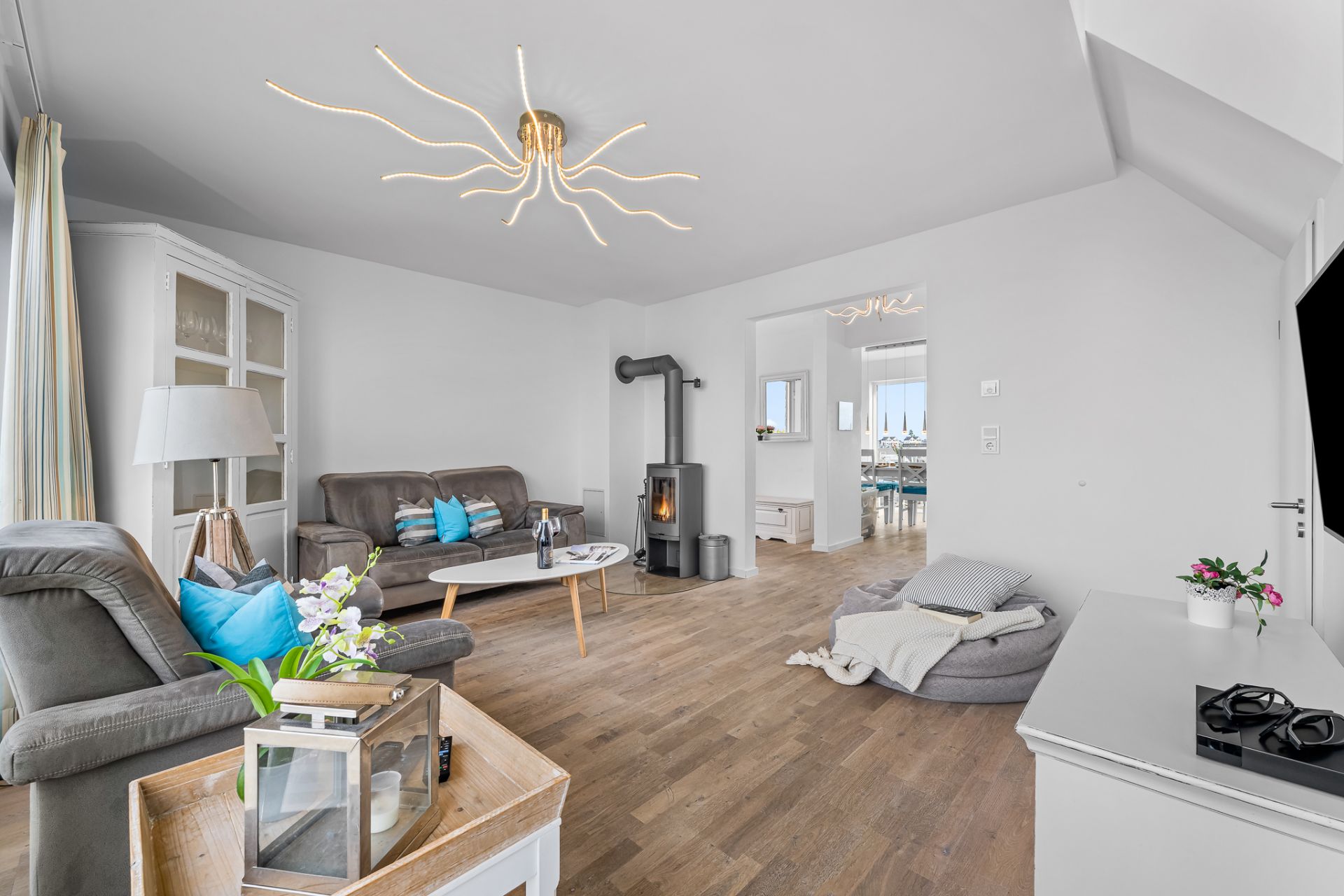 Helles Wohnzimmer mit grauen Sofas, Holzofen, Holzfußboden und modernen Lampen.