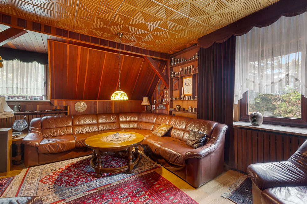 Wohnzimmer mit großer brauner Ledercouch, Holztisch, Teppich und Holzdecke.