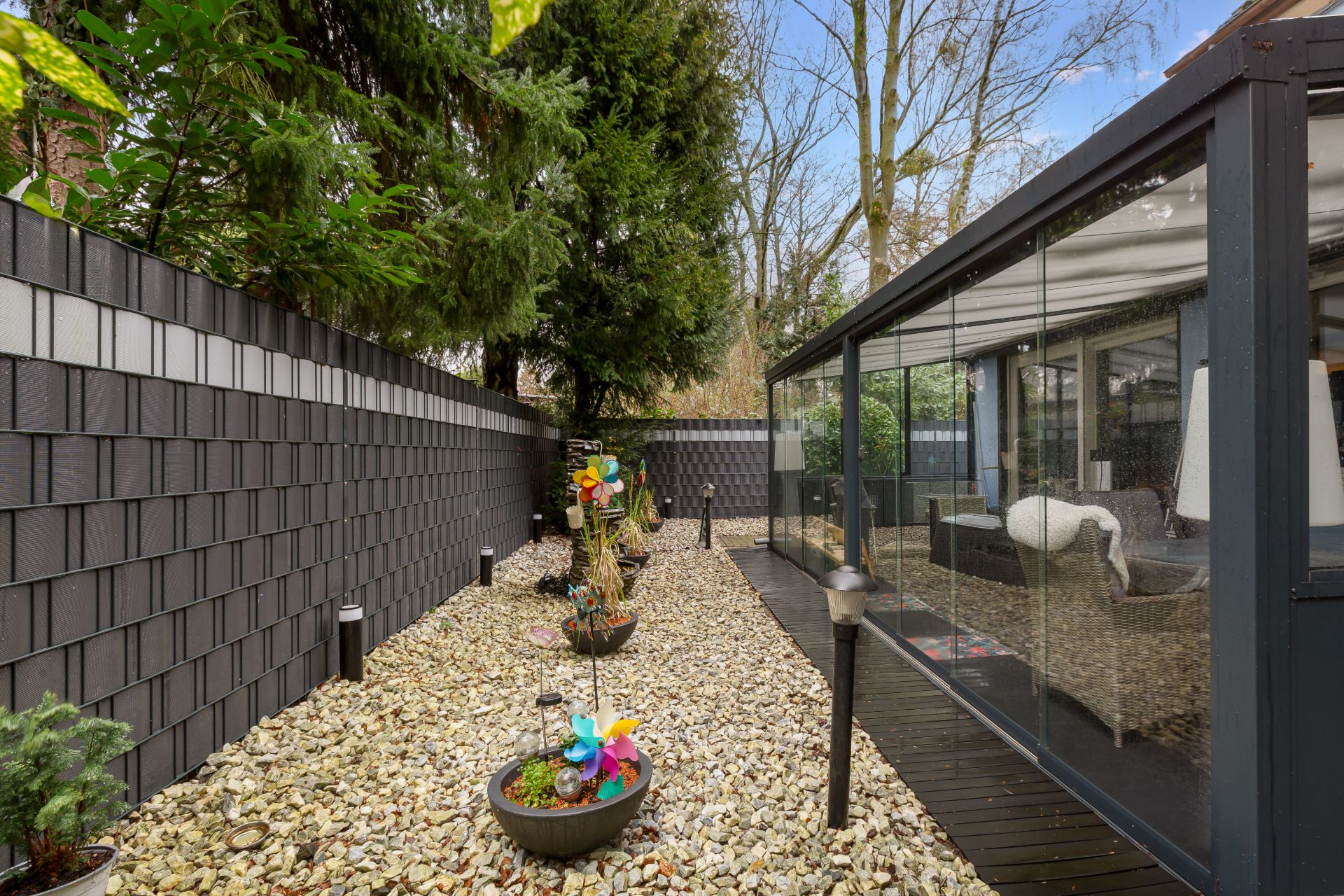 Steingarten mit Pflanzgefäßen und Windspielen neben verglaster Terrasse.