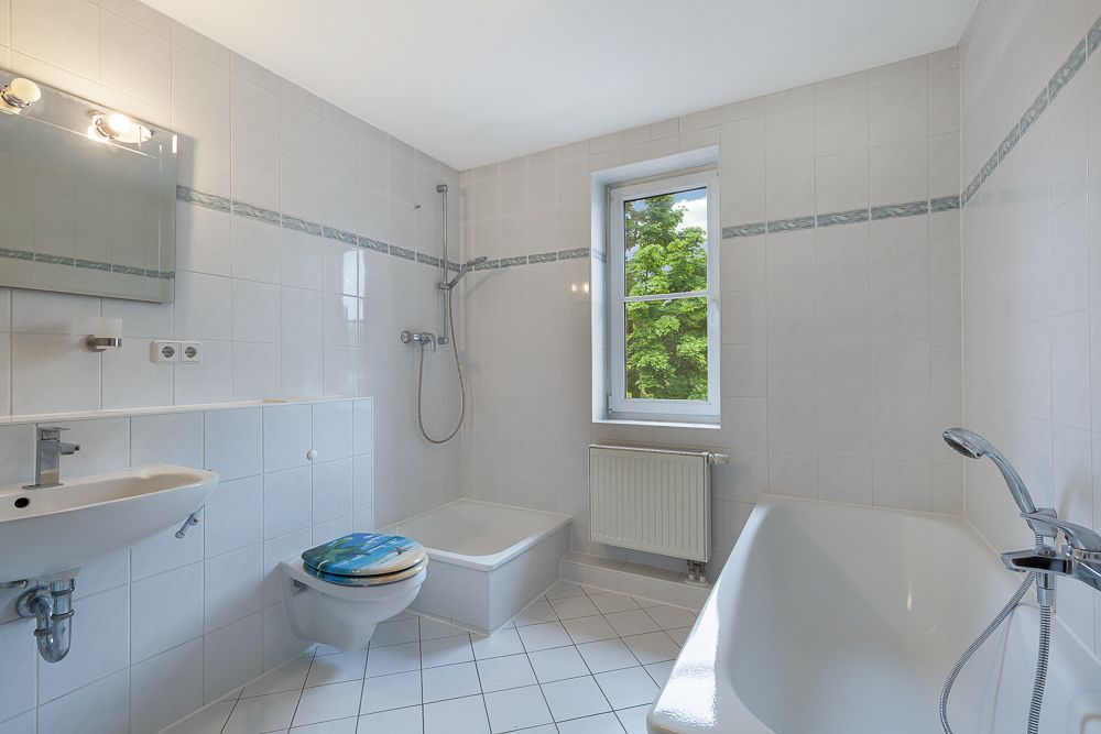 Helles Badezimmer mit Badewanne, Dusche, Waschbecken, Toilette und Fenster.