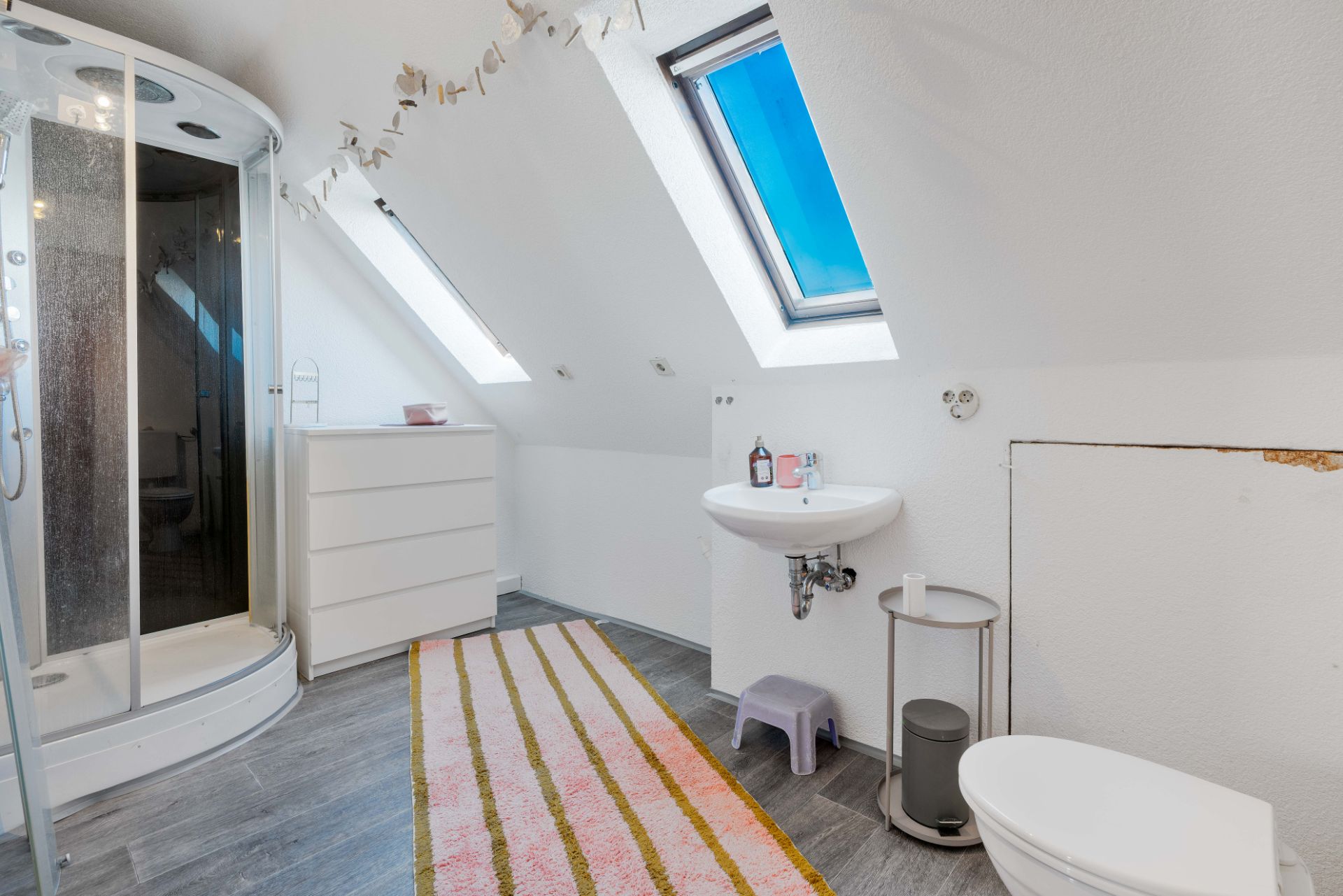Modernes Badezimmer mit Dusche, Waschbecken, Toilette, Kommode und Dachfenstern.