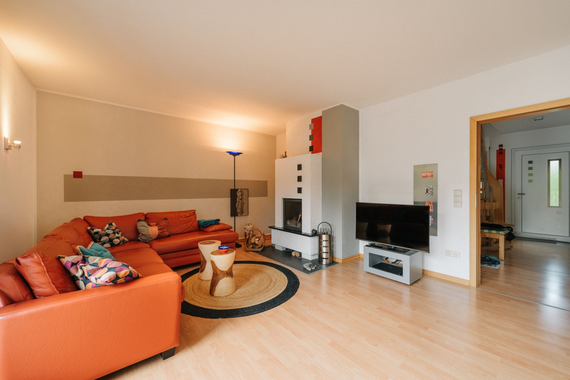 Modernes Wohnzimmer mit orangefarbenem Sofa, rundem Teppich und Fernseher, Holzfußboden.
