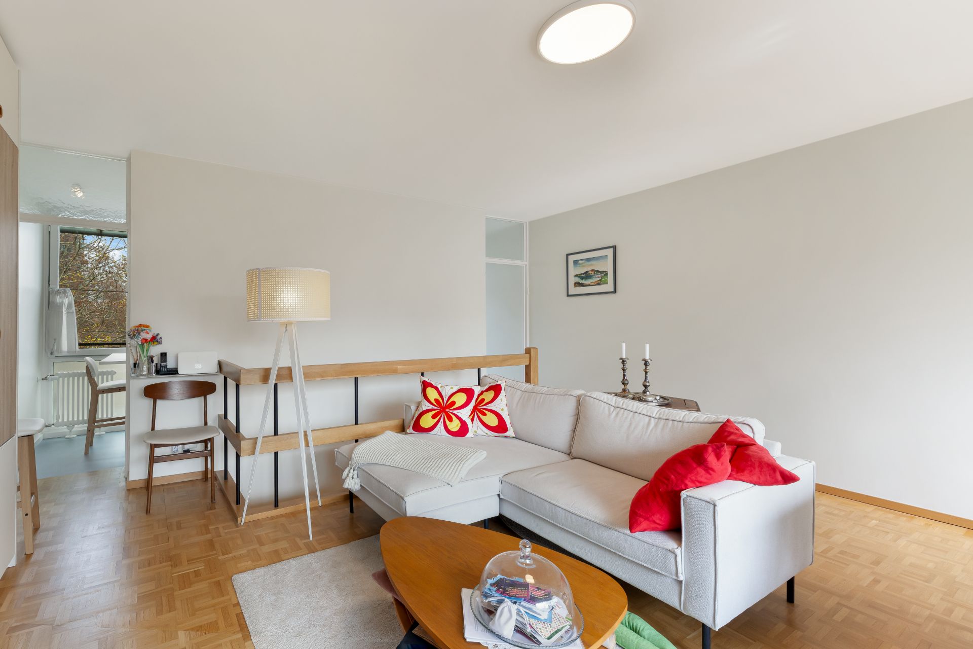 Helles Wohnzimmer mit Ecksofa, Stehlampe, Couchtisch und Esstisch am Fenster.