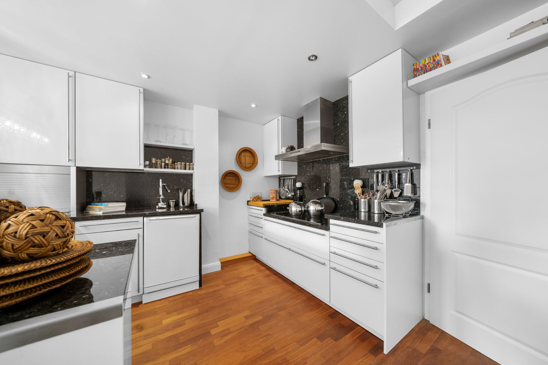 Moderne weiße Küche mit Holzfußboden, schwarzen Arbeitsplatten und Hängeschränken.