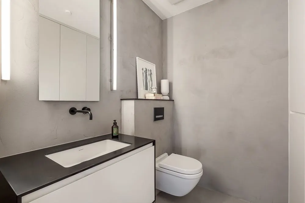 Modernes Badezimmer mit Waschbecken, Hängespiegel, Wandtoilette und grauen Wänden.