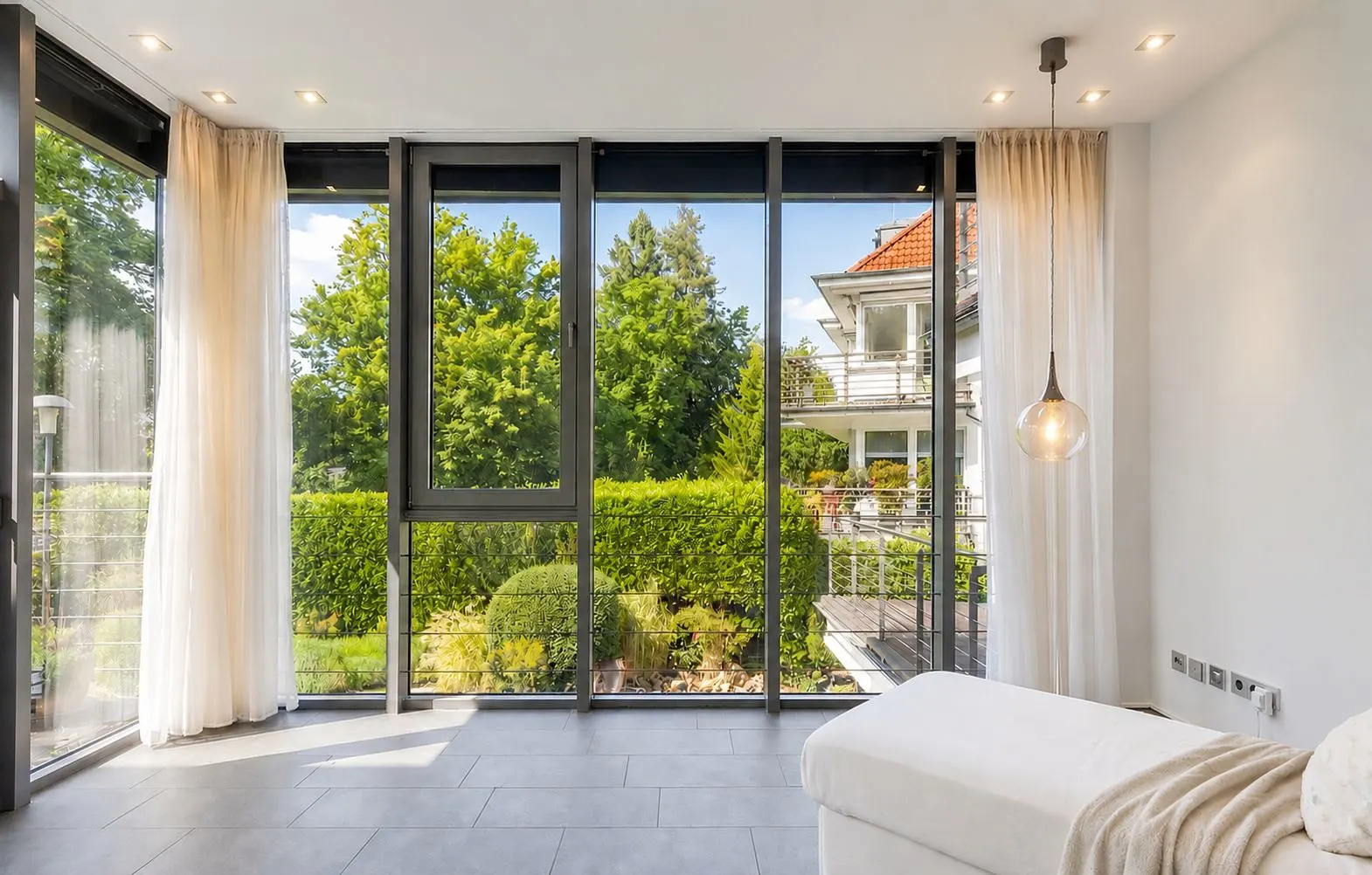 Helles Zimmer mit großen Fensterfronten, Blick auf Garten und Nachbarhaus, modern eingerichtet.